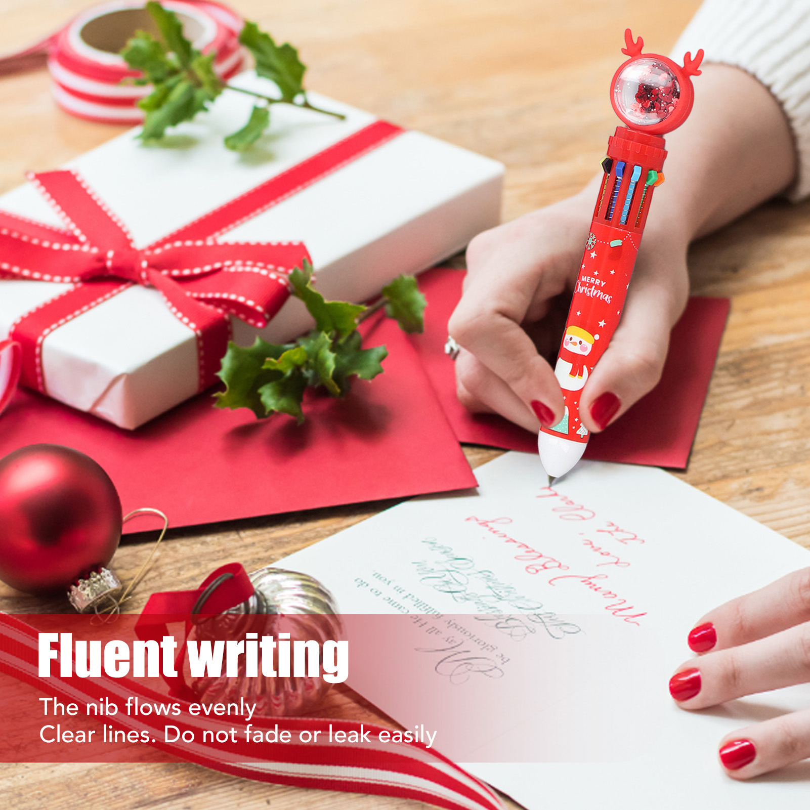 Eine Hand schreibt mit einem Weihnachtskugelschreiber auf eine Karte. Geschenk, Ornamente und Bänder auf Holzoberfläche.