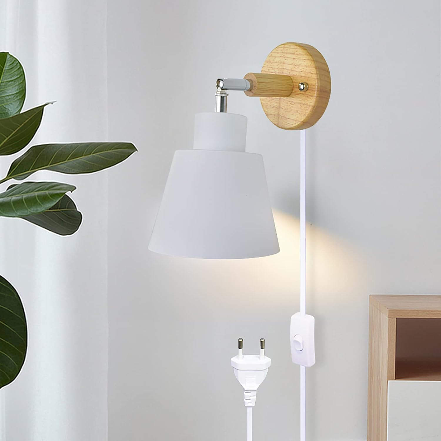 Eine weiße Wandlampe mit Holzsockel ist an einer weißen Wand montiert. Ein weißes Stromkabel mit Schalter und Stecker ist sichtbar.