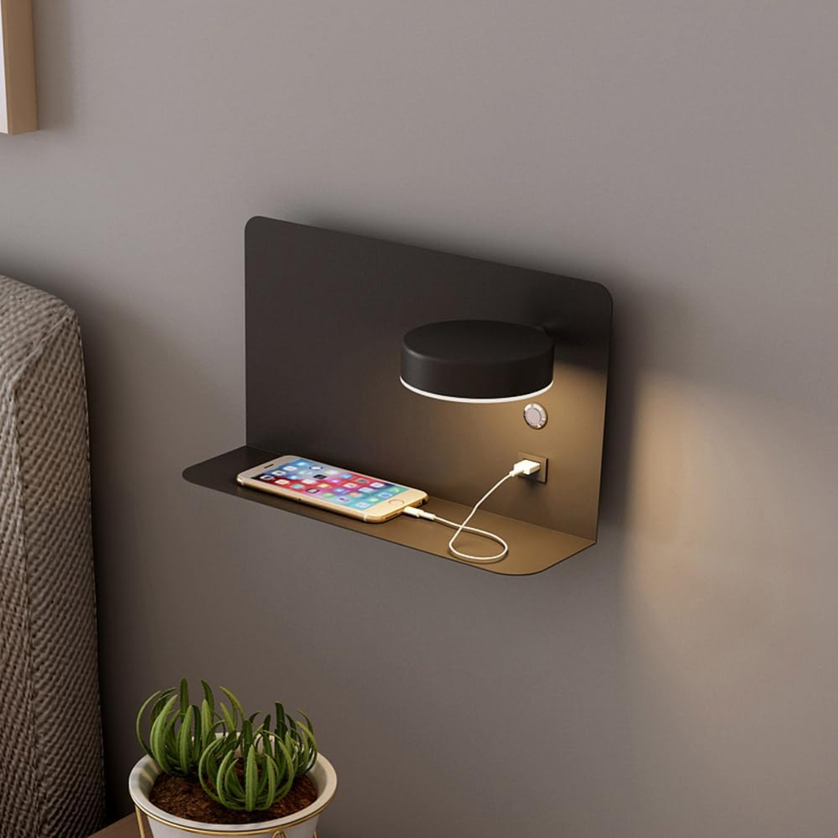 Ein moderner Nachttisch mit Lampe, Ablage und Telefonladung. Auf der Ablage befindet sich ein Telefon, das mit dem Ladegerät verbunden ist. Darunter steht eine Pflanze.