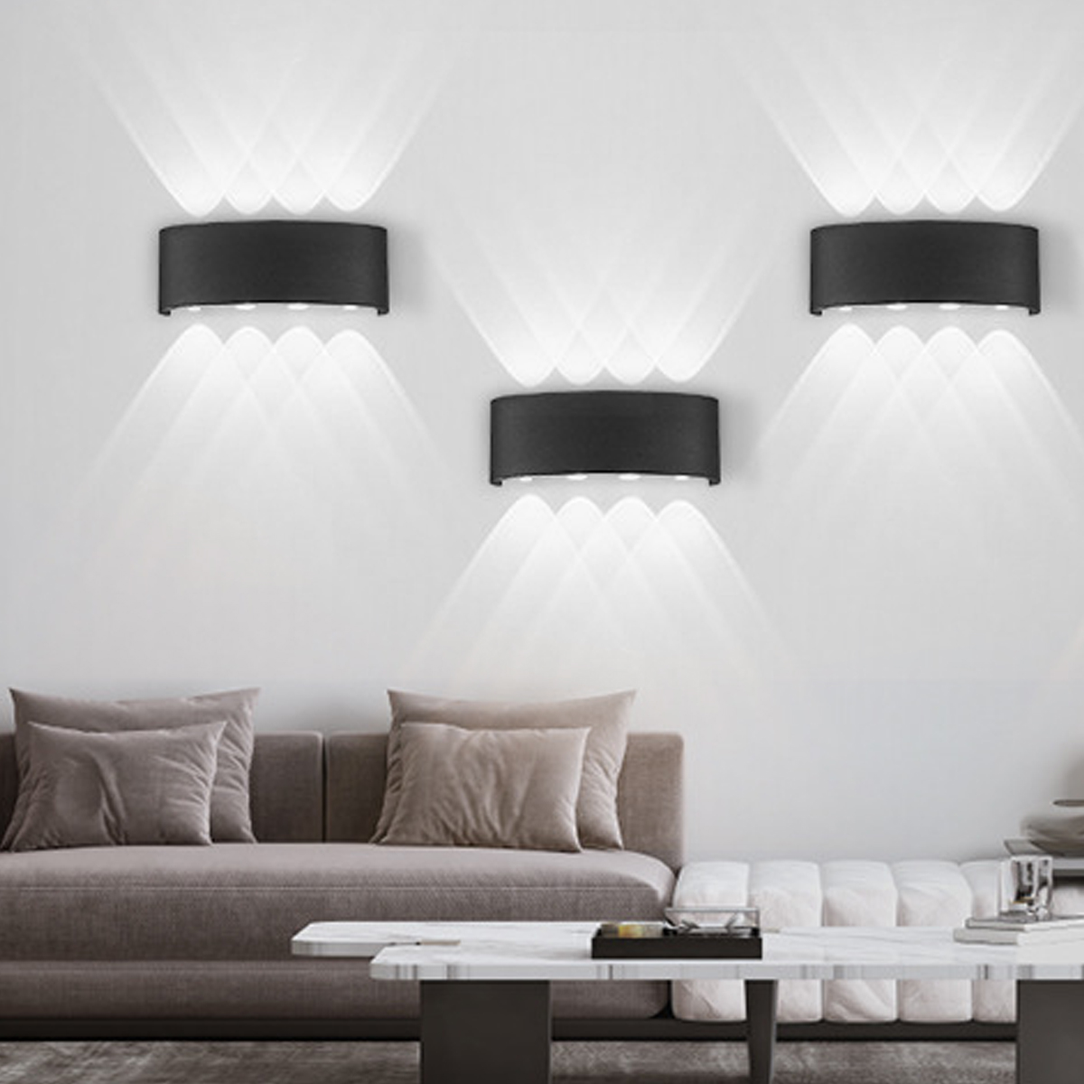 Drei schwarze Wandlampen beleuchten eine weiße Wand. Ein graues Sofa und ein Couchtisch befinden sich im Vordergrund.
