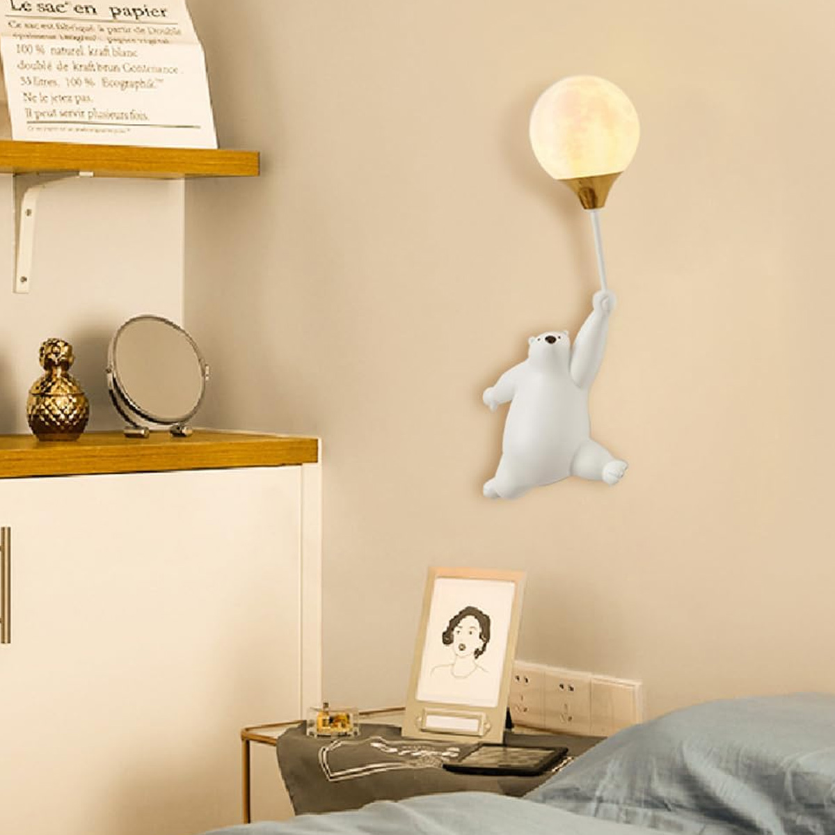 Eine Eisbärlampe, die ein mondförmiges Licht hält. Neben einem Schreibtisch mit Gegenständen, einem Bilderrahmen, einem Bett und einer Papiertüte.