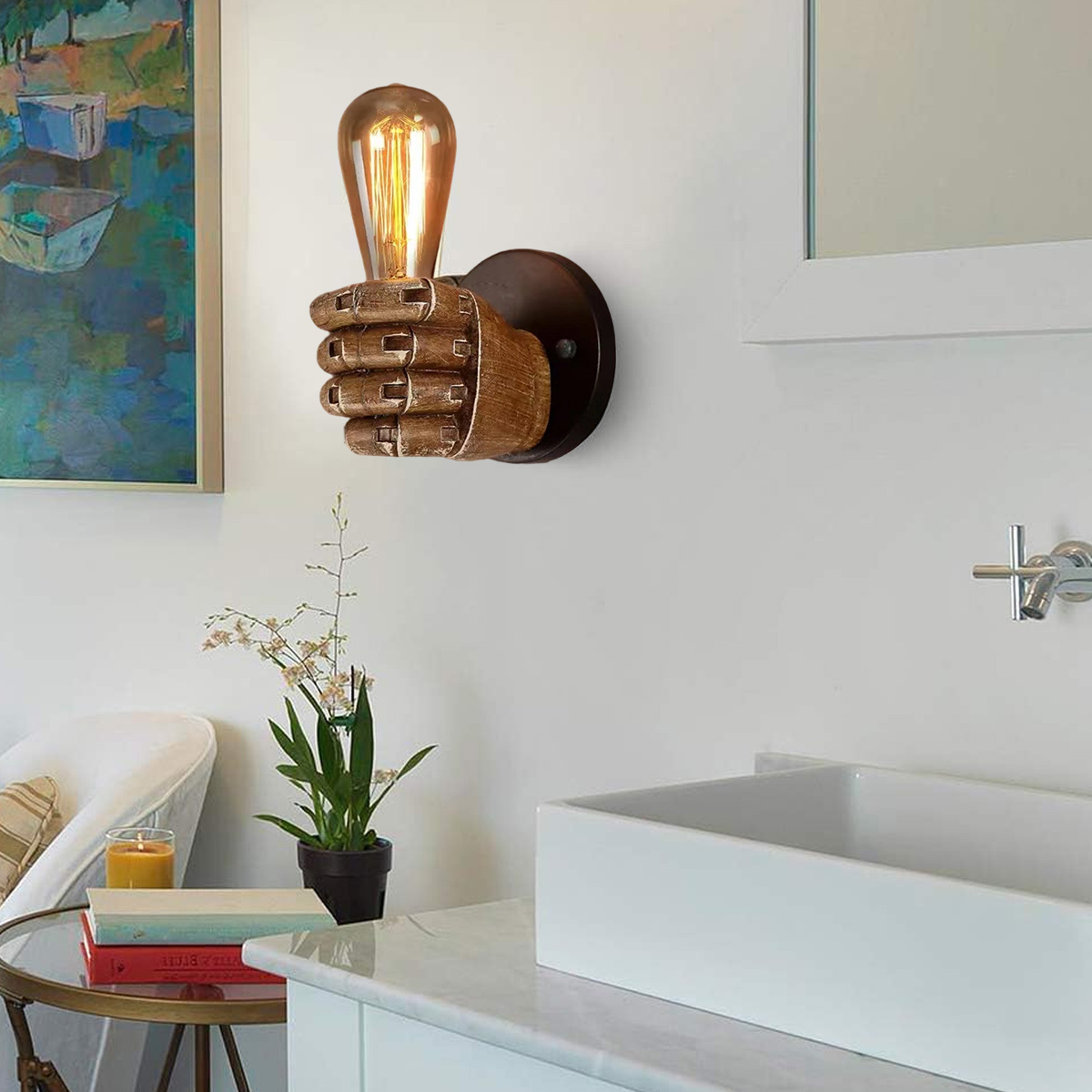 Eine handförmige Wandlampe mit Glühbirne, an einer weißen Wand befestigt. Ein Gemälde und Badezimmerarmaturen sind ebenfalls sichtbar.