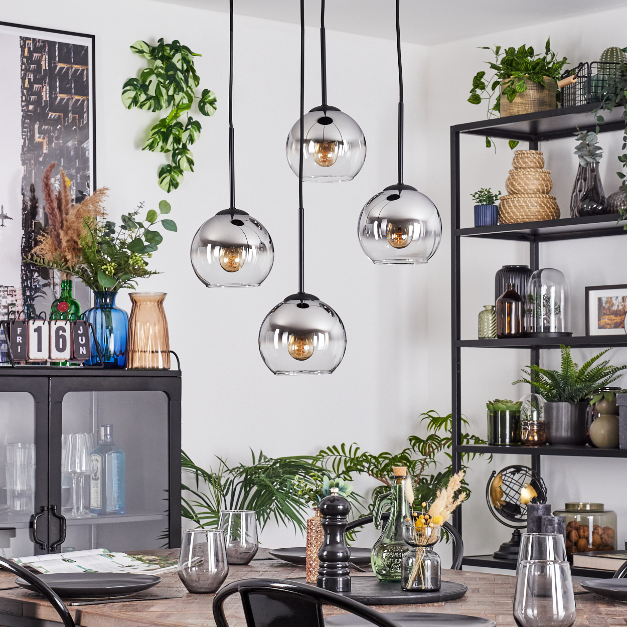 Esszimmer mit vier kugelförmigen Pendelleuchten, Tisch mit Tellern und Gläsern, Pflanzen auf Regalen.