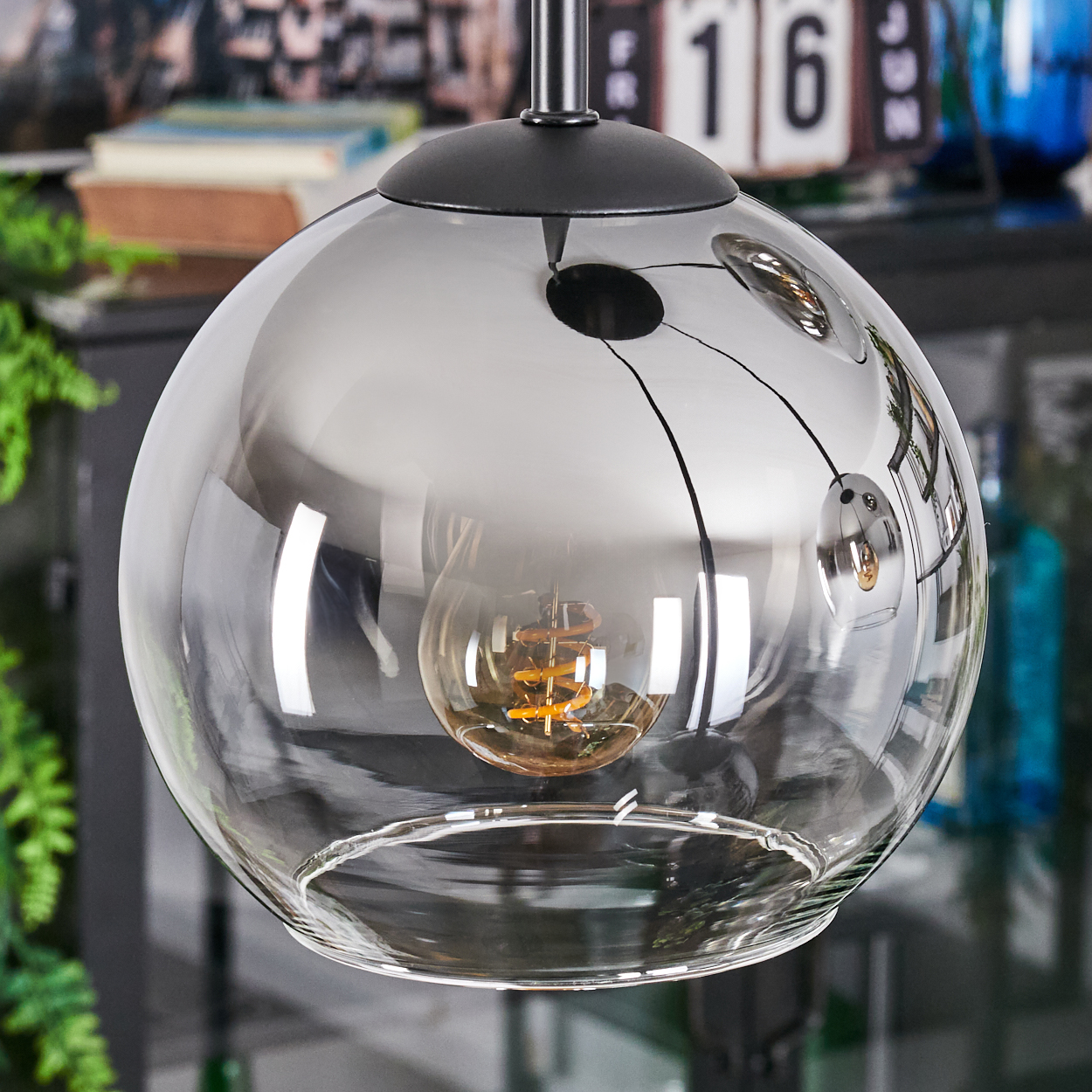 Eine moderne Glaskugellampe mit sichtbarer Glühbirne. Die Kugel spiegelt die Umgebung. Die Lampe hängt von der Decke.
