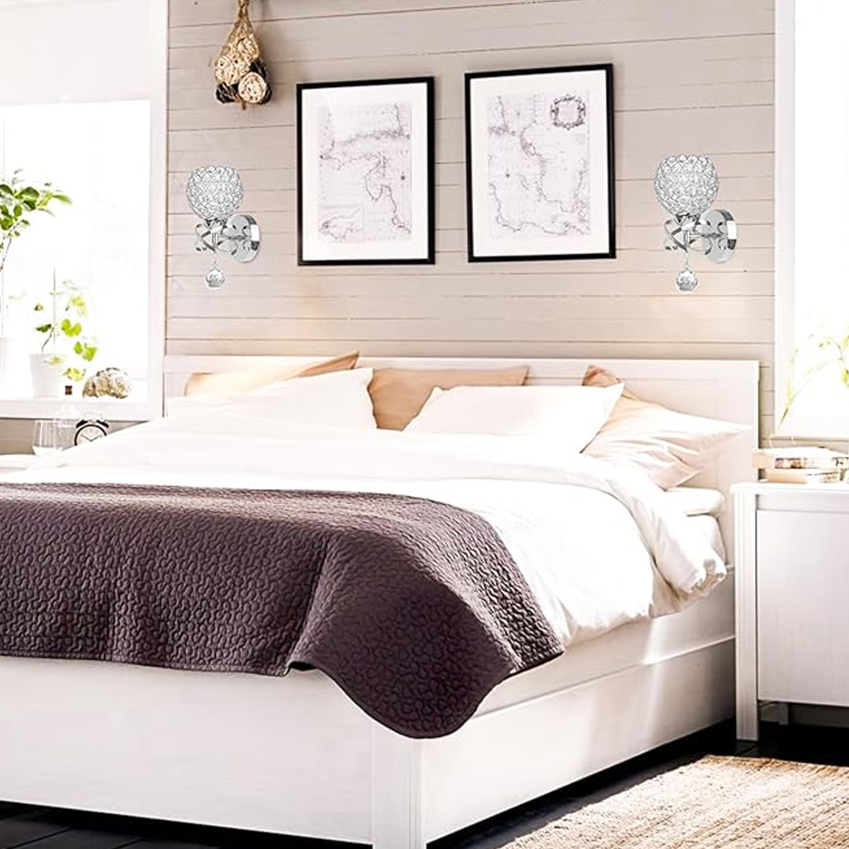 Schlafzimmer mit Bett, Lampen und Wandkunst. Bett hat weiße Bettwäsche und eine braune Steppdecke. Zwei gerahmte Karten an der Wand.