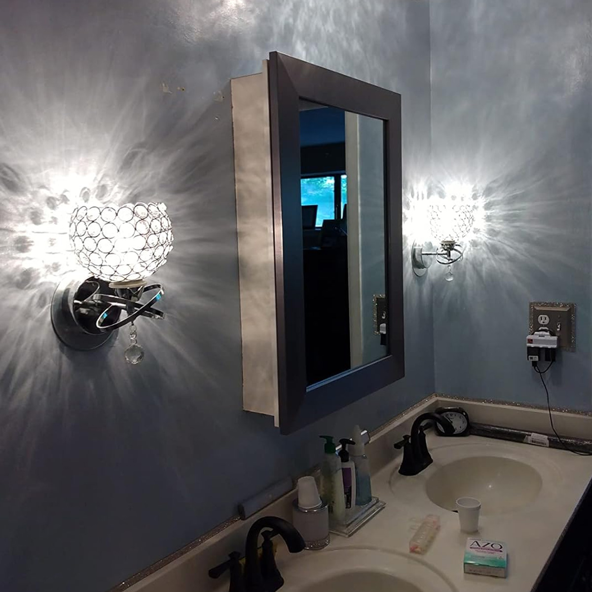 Badezimmer mit Spiegel, zwei Waschbecken und dekorativen Wandleuchten. Blaue Wände, weiße Arbeitsplatte und schwarze Armaturen.