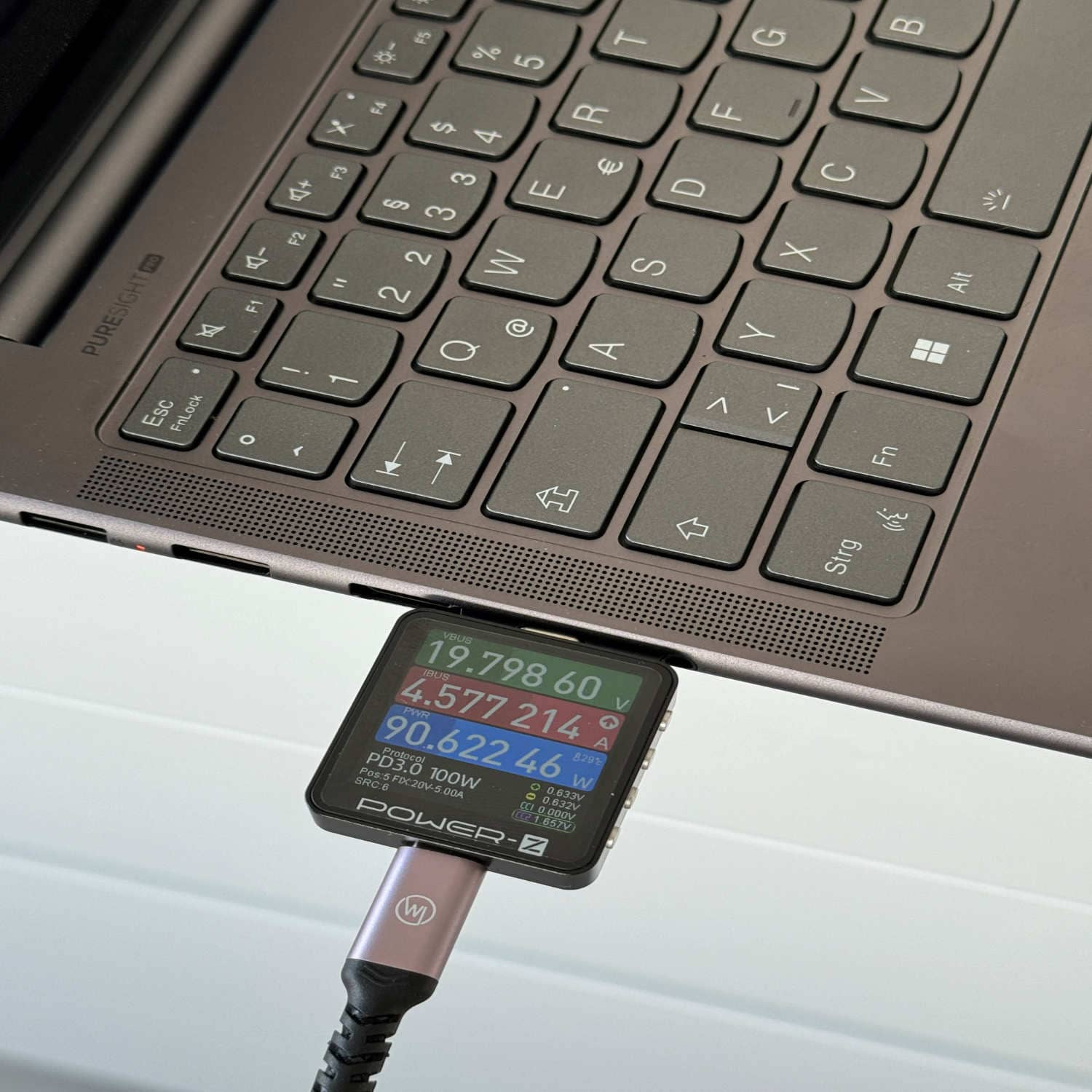 Laptop-Tastatur mit angeschlossenem Leistungsmesser, der Spannungs-, Strom- und Wattwerte anzeigt.