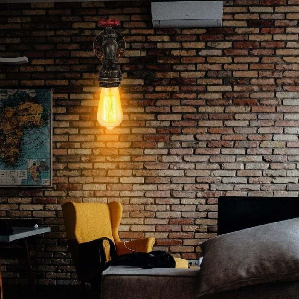 Eine rustikale Wand mit einer Leuchte und einer Karte. Davor steht ein gelber Stuhl. Ein Kissen und ein Tisch sind ebenfalls sichtbar.