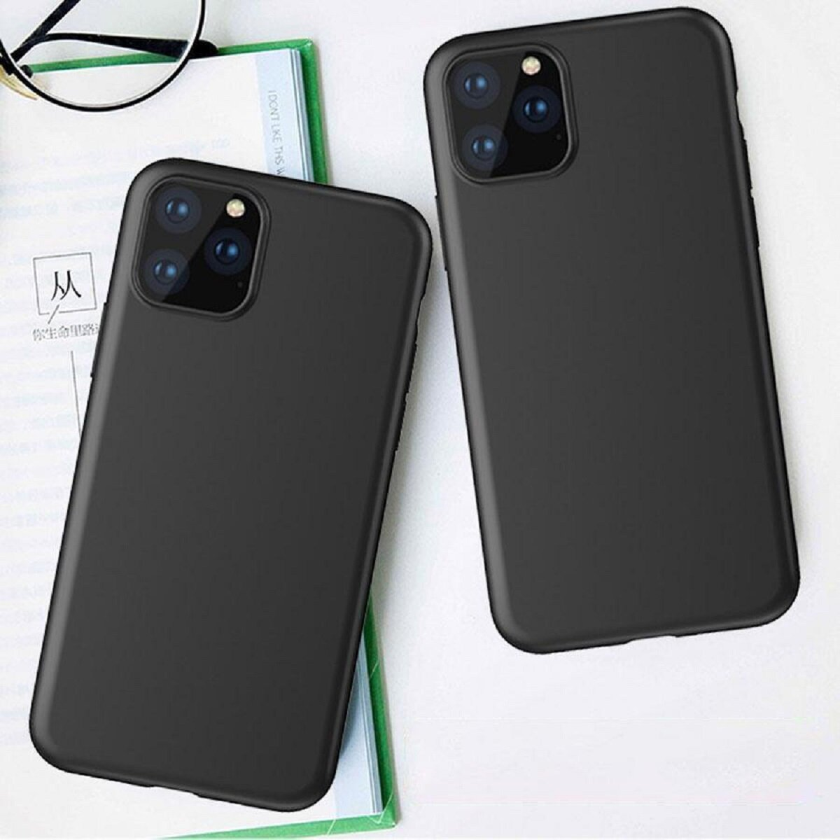 Zwei schwarze Smartphone-Hüllen liegen auf einer weißen Oberfläche mit einem Buch und einer Brille. Jede Hülle hat ein Kameramodul.