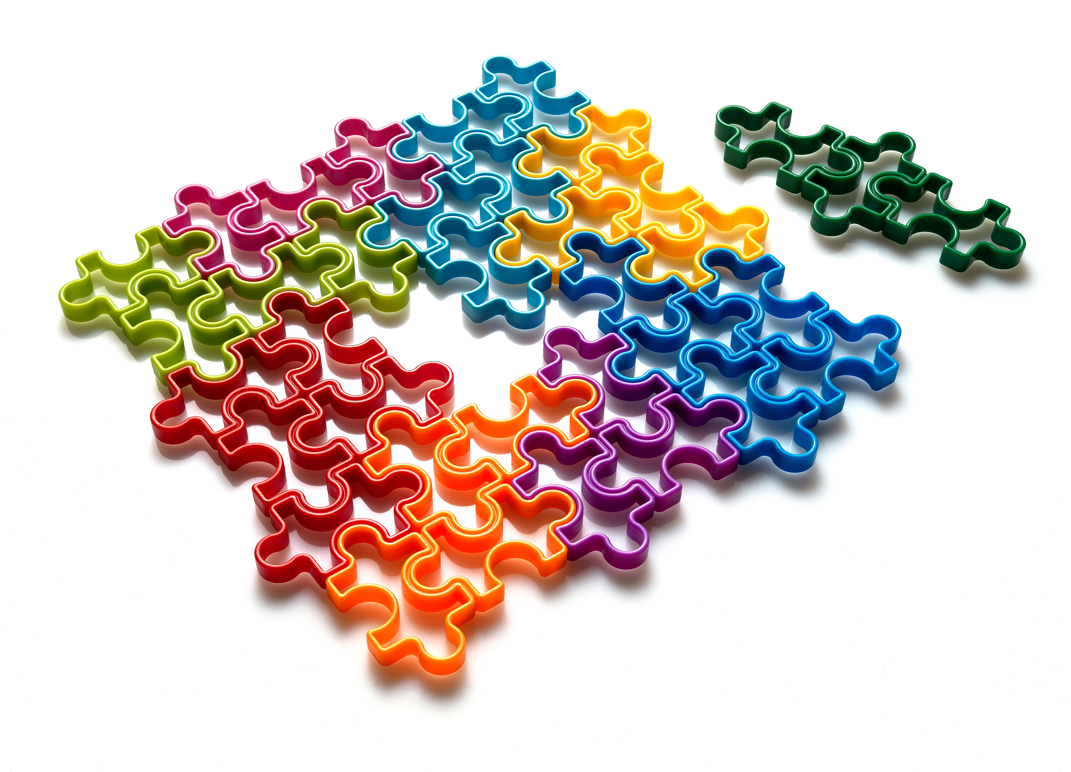 Kolorowe elementy układanki na białym tle, niektóre połączone, inne osobno. Kolory to zielony, czerwony, pomarańczowy, fioletowy itp.