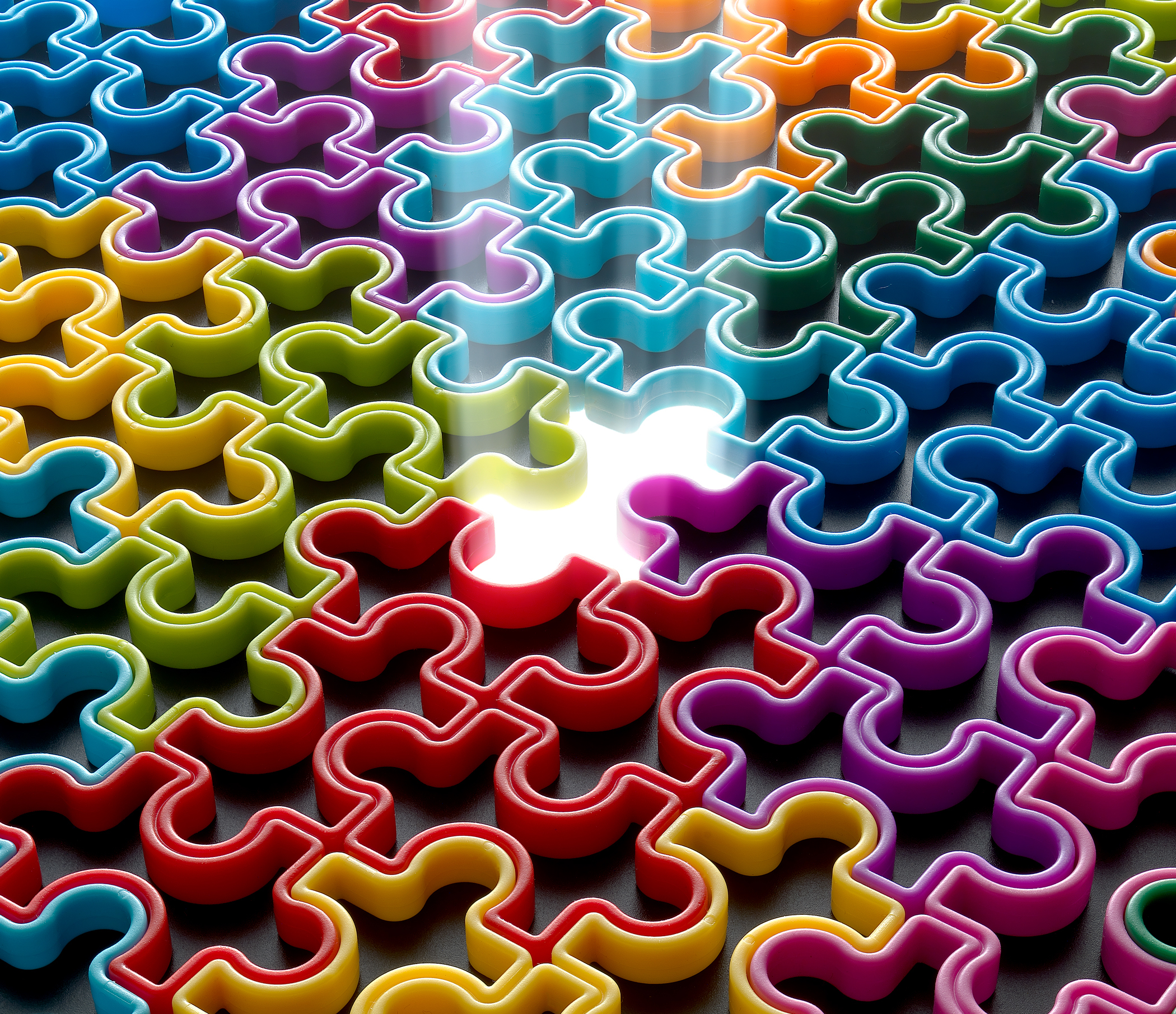 Kolorowe elementy układanki, jeden brakuje, emitujący światło. Elementy są czerwone, niebieskie, zielone, żółte, pomarańczowe i fioletowe.