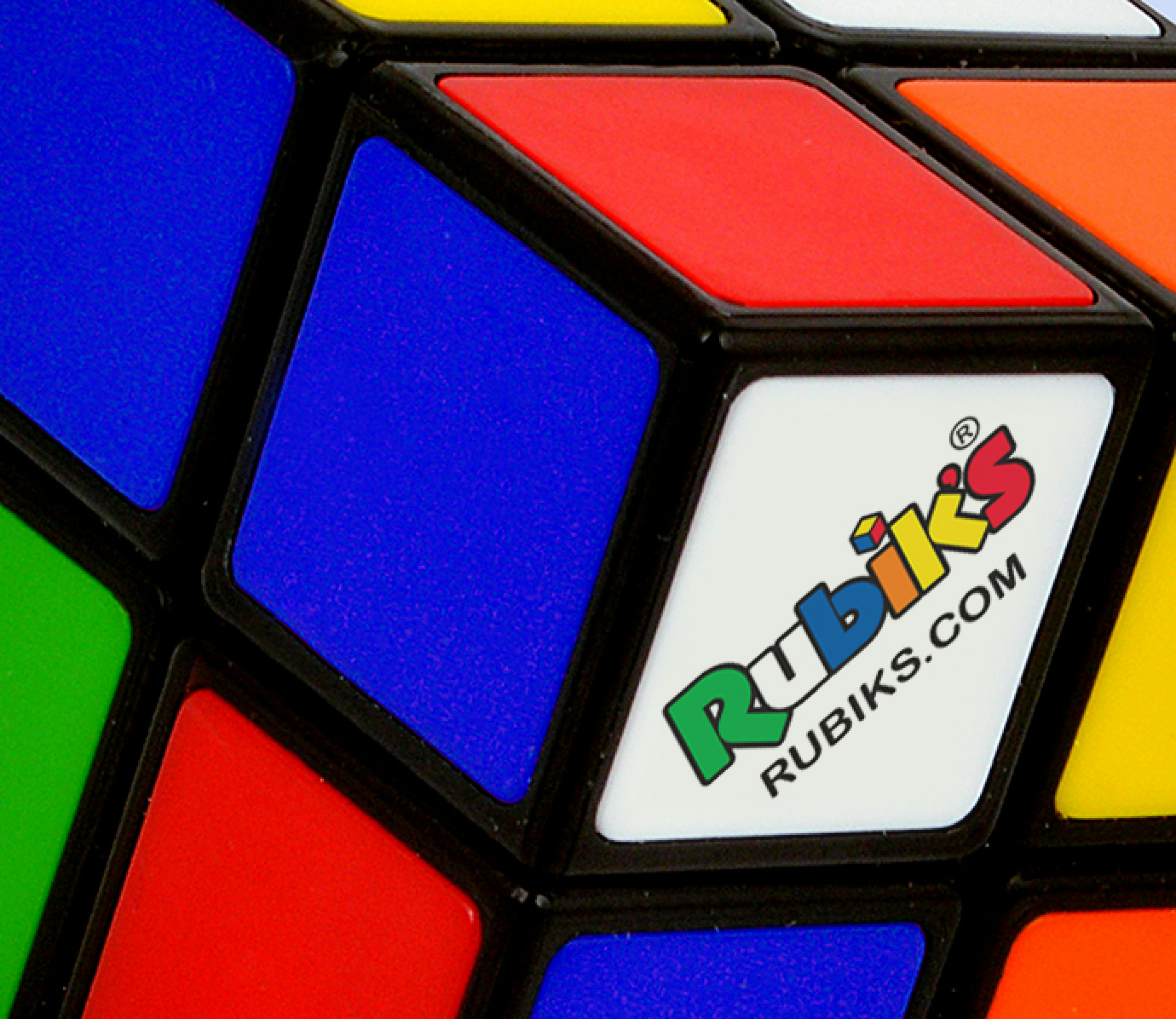 Nahaufnahme eines Zauberwürfels. Sichtbare Flächen sind blau, rot, weiß mit Rubik's Logo, gelb, grün und orange.