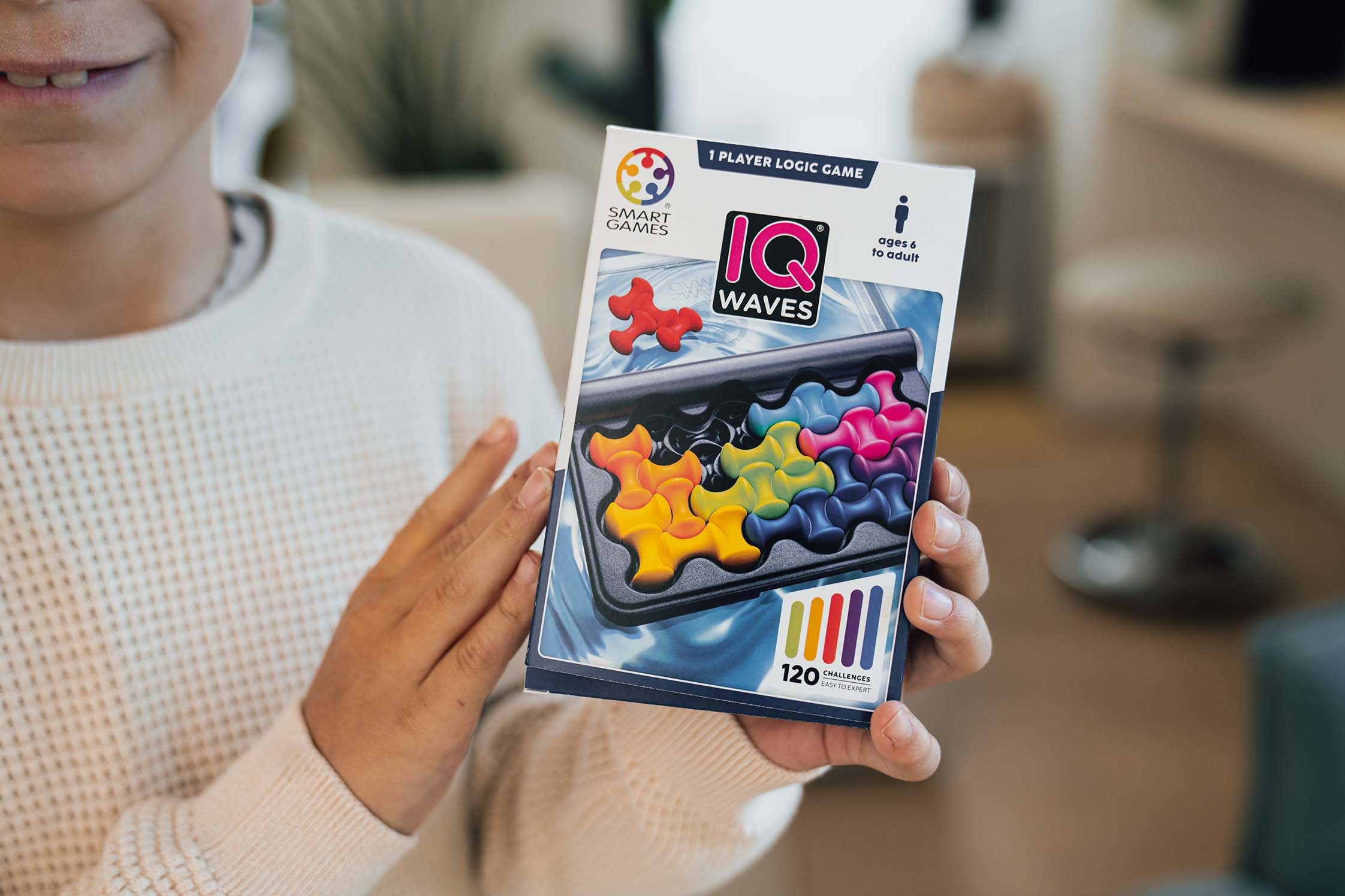 Eine Person hält eine Puzzlespielbox. Die Box zeigt bunte Puzzleteile und den Namen des Spiels IQ Waves.