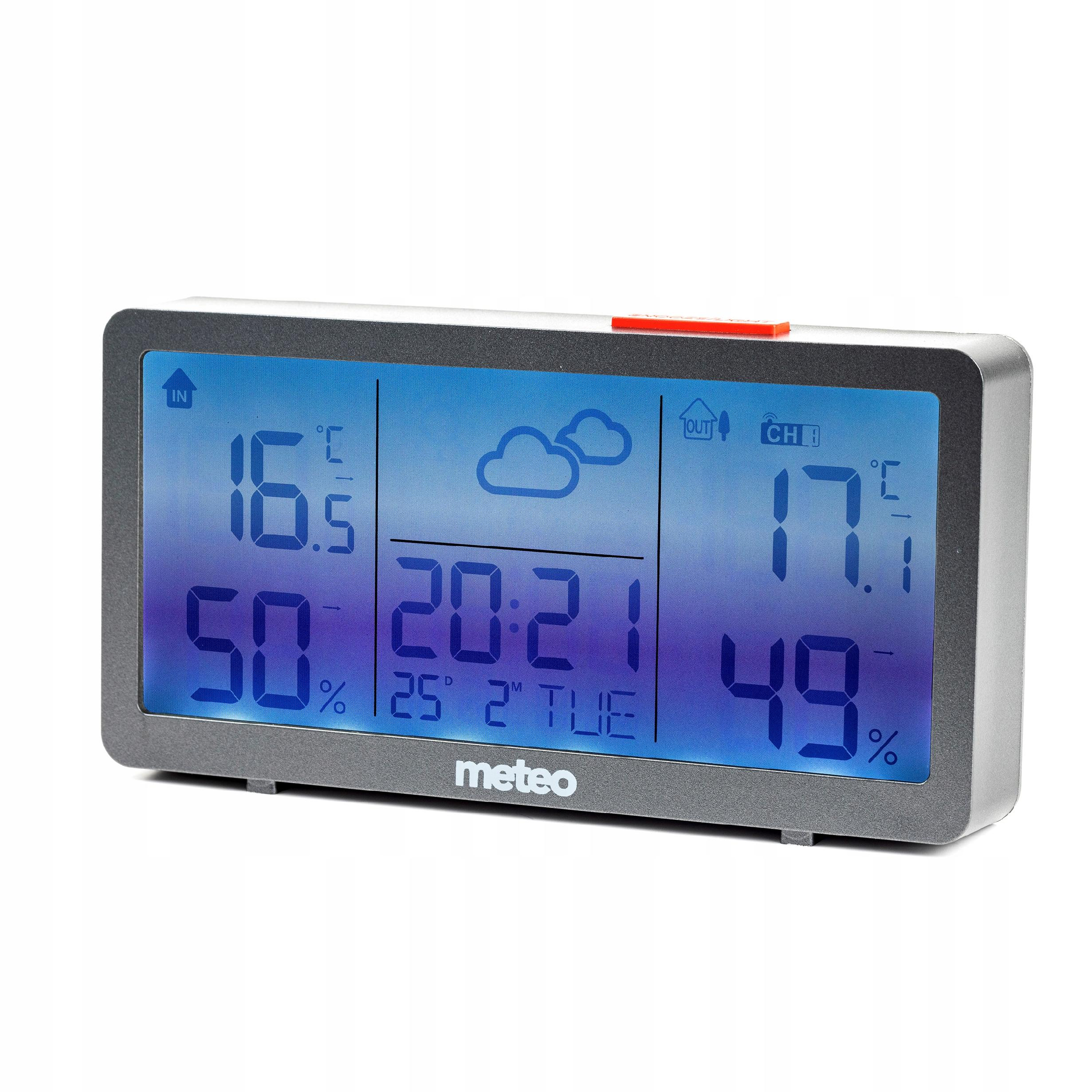 Cyfrowa stacja pogodowa wyświetla temperaturę wewnątrz/na zewnątrz, godzinę, datę i wilgotność. Ma niebieski ekran i szarą ramkę.