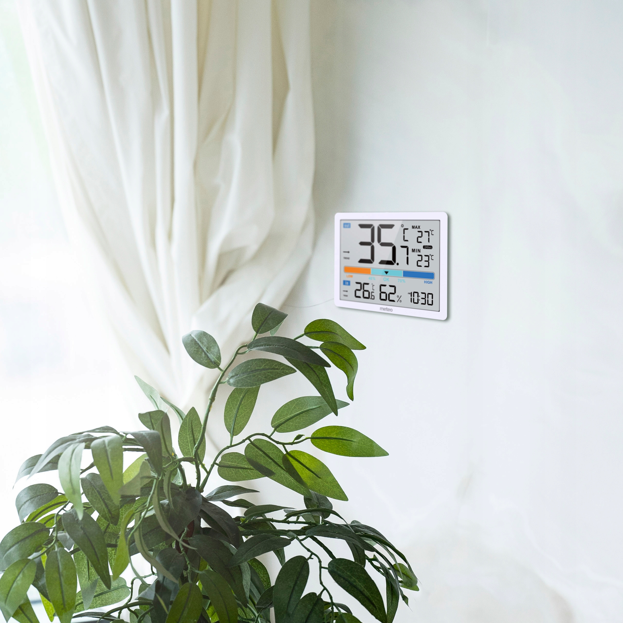 Biała ściana z termometrem, zieloną rośliną i białym zasłoną.