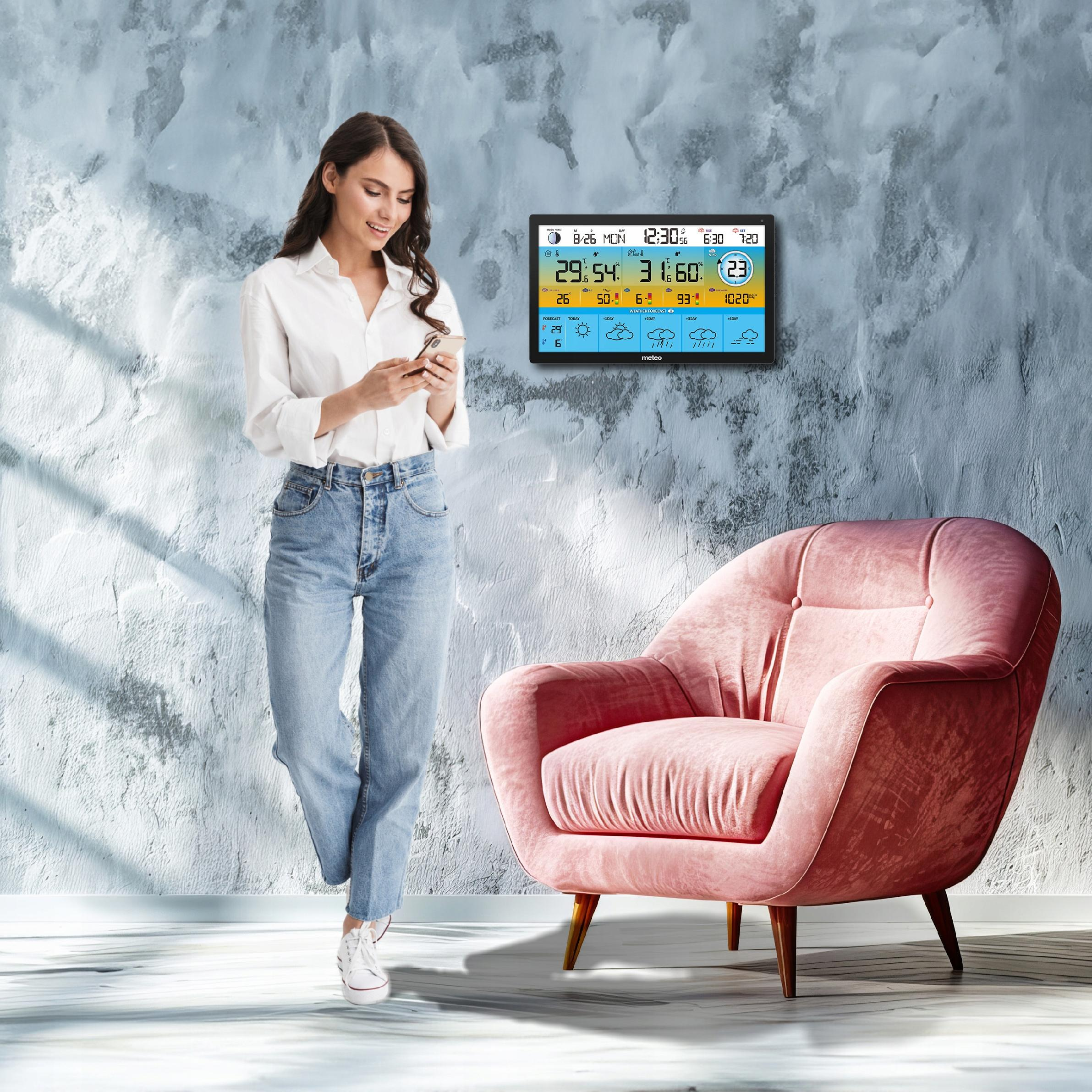 Kobieta w białej koszuli i dżinsach trzymająca telefon stoi obok różowego krzesła w pobliżu wyświetlacza pogody.