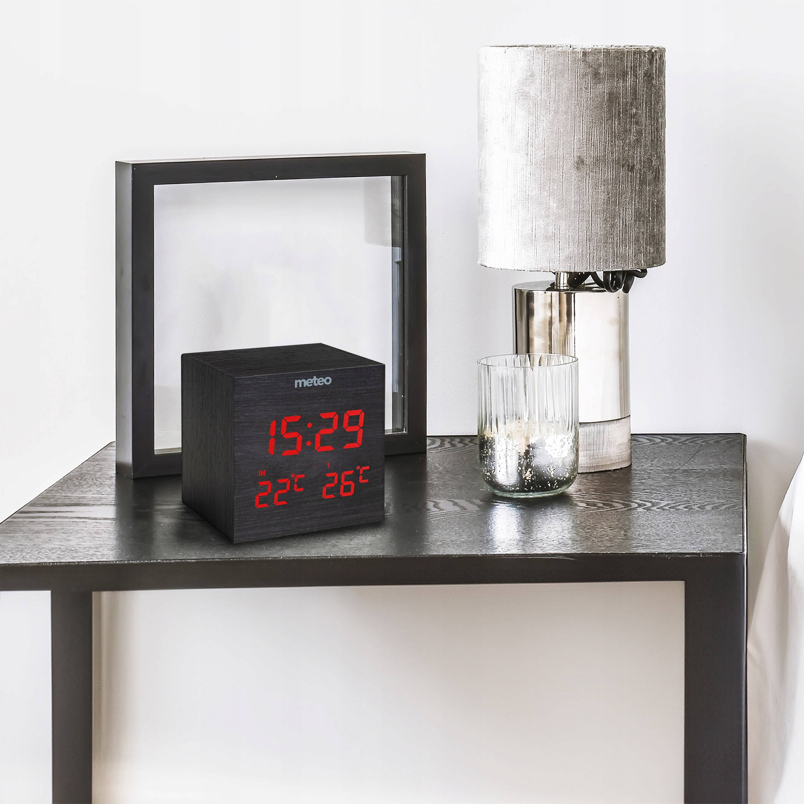 Szafka nocna z zegarem, lampą i szklanką. Zegar wyświetla godzinę i temperaturę.