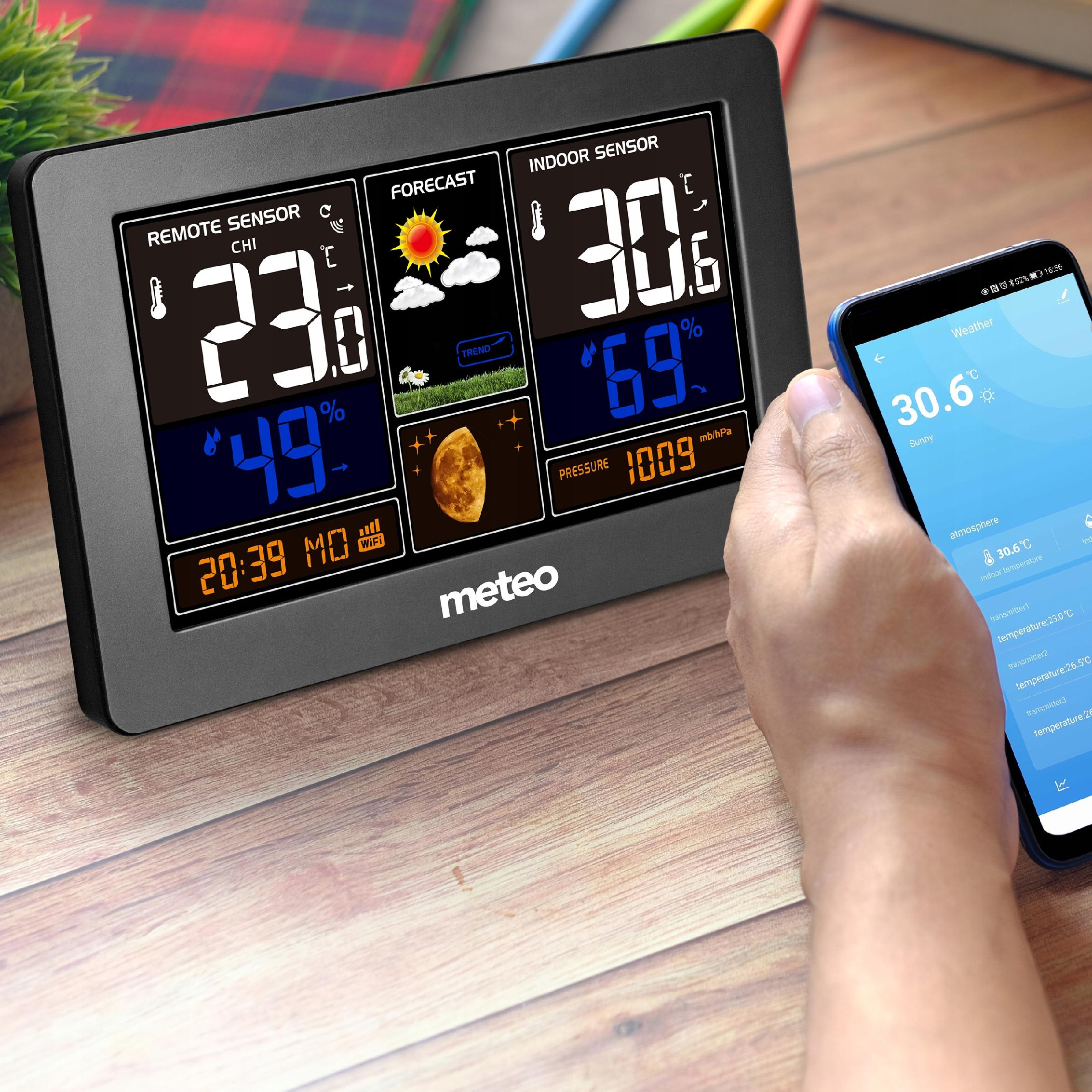 Stacja pogodowa wyświetla odczyty obok telefonu pokazującego te same dane. Stacja pokazuje temperaturę, wilgotność i prognozę.