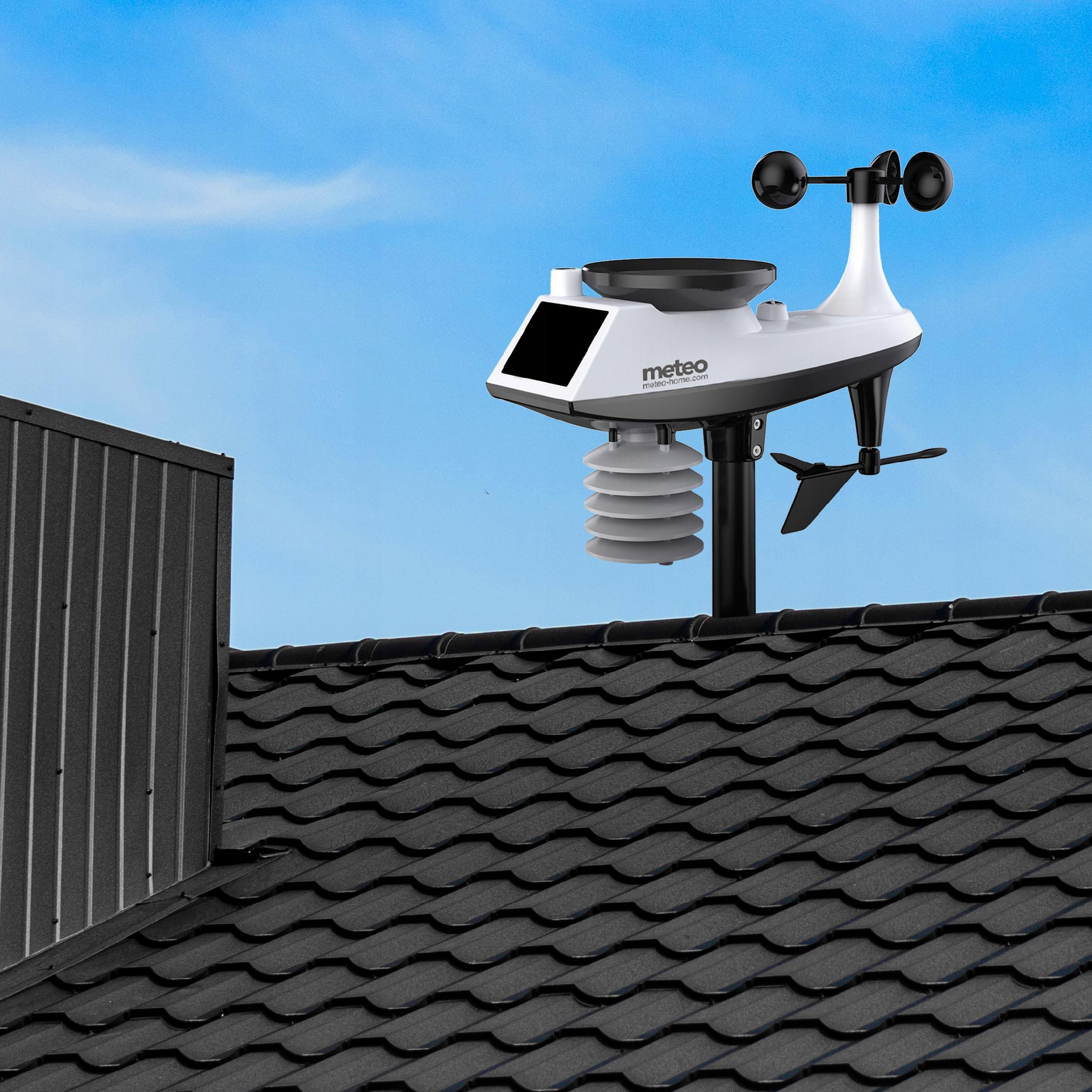 Stacja pogodowa na dachu na tle błękitnego nieba. Dach jest czarny. Stacja jest biało-czarna.