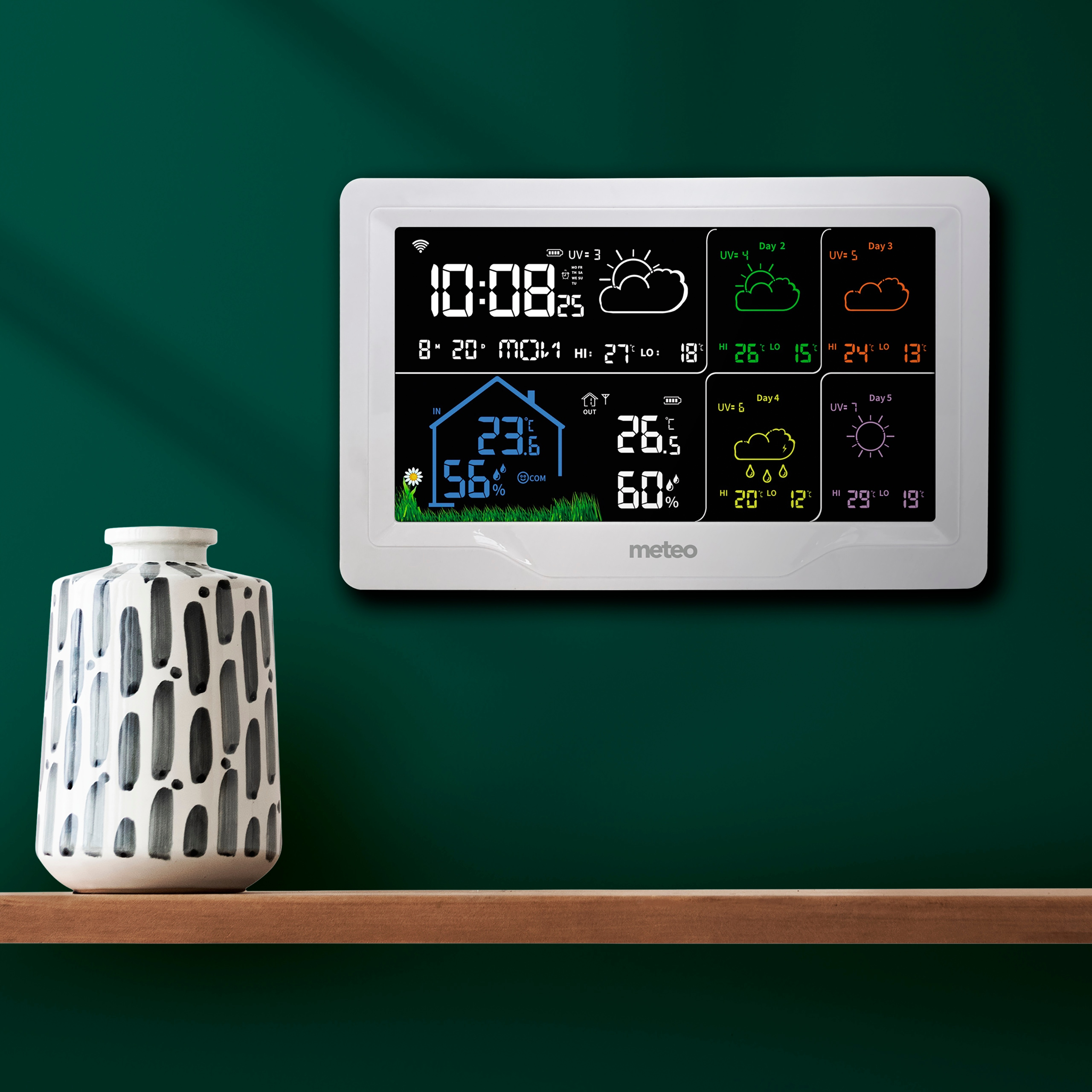 Stacja pogodowa wyświetla czas, temperaturę wewnątrz/na zewnątrz i prognozy pogody. Wazon na drewnianej półce.