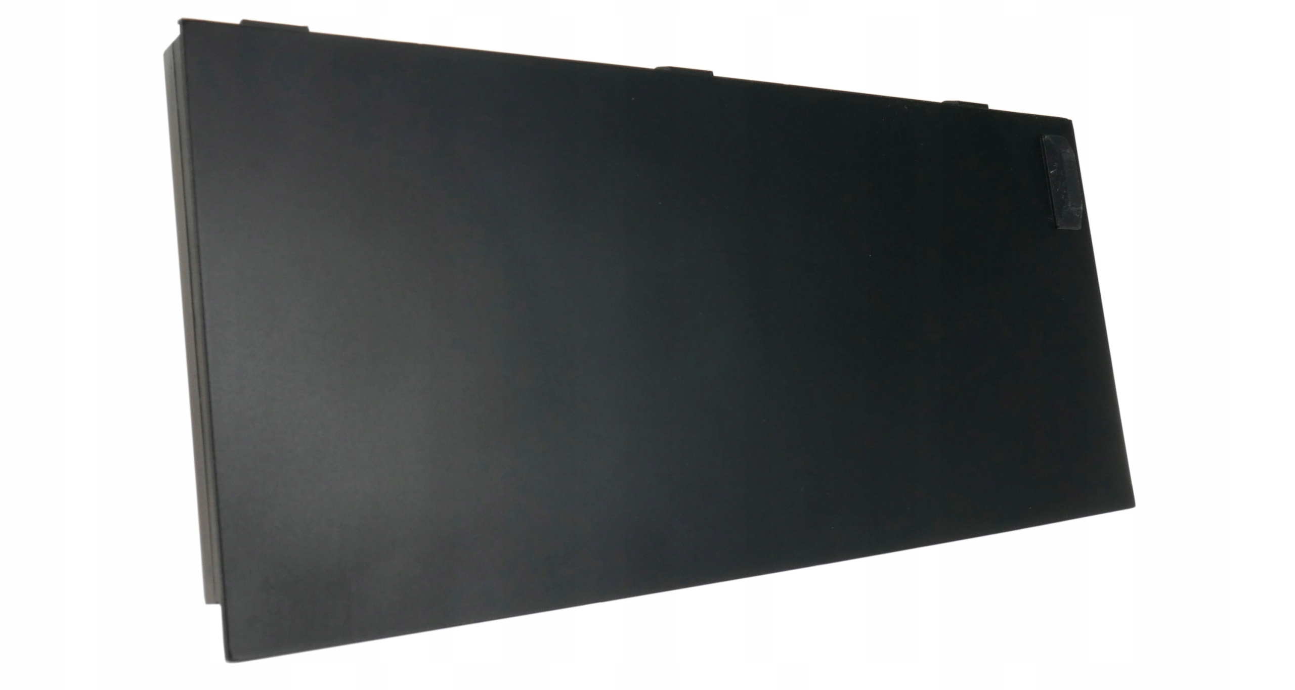 Czarny prostokątny obiekt, lekko pochylony, na białym tle. Ma małe wypustki na górze i naklejkę.