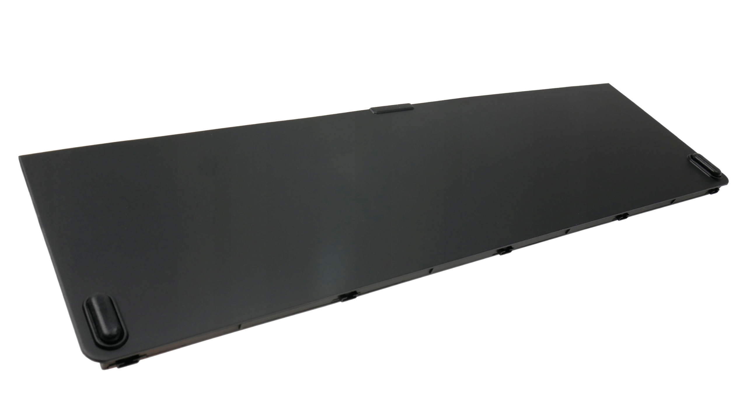 Czarny element laptopa, prawdopodobnie pokrywa, leży na białej powierzchni. Jest prostokątny, z zaokrąglonymi rogami i małymi mocowaniami.