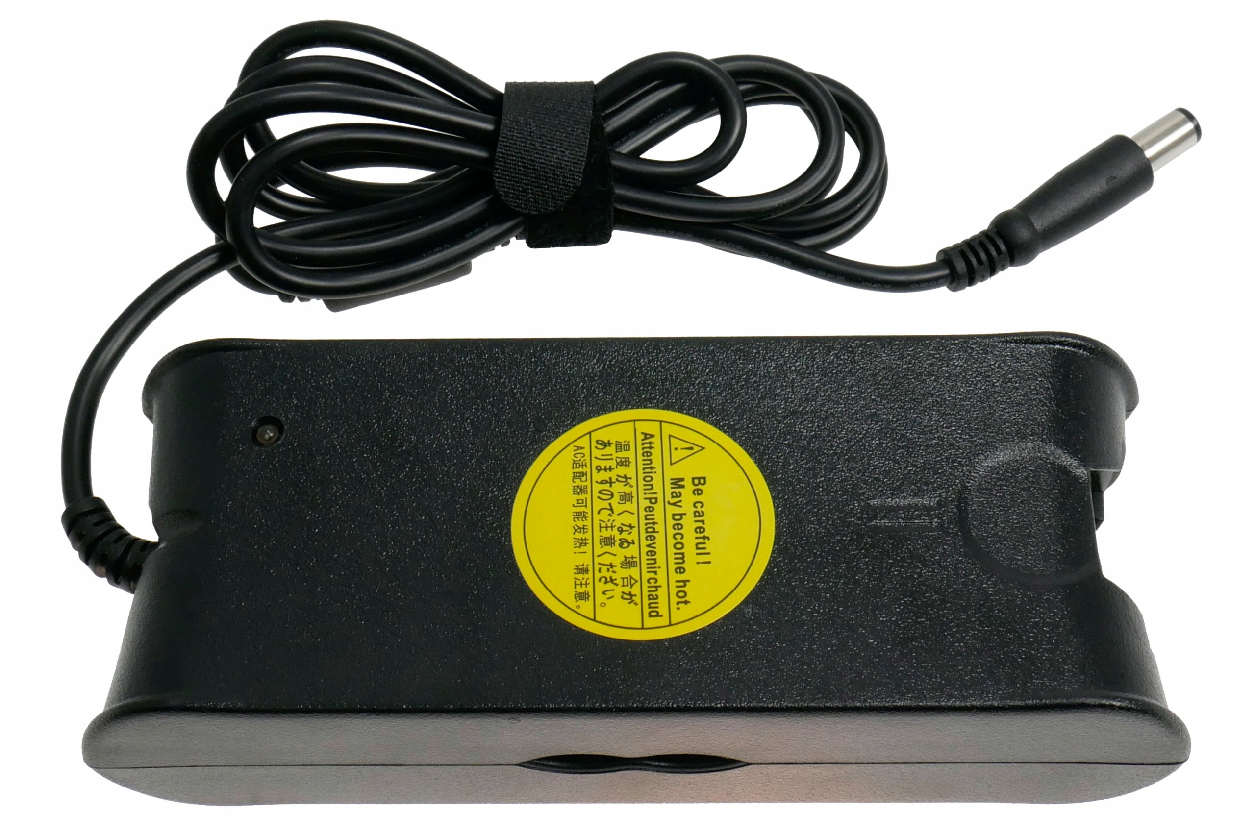Czarna ładowarka do laptopa z czarnym kablem. Widoczna jest żółta etykieta ostrzegawcza. Kabel jest owinięty czarnym rzepem.