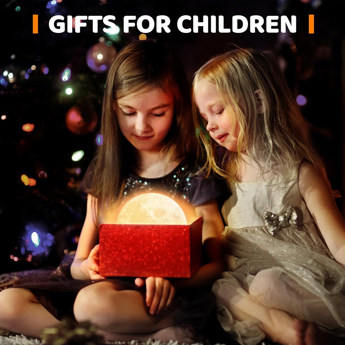 Zwei Mädchen betrachten eine rote Geschenkbox mit einem leuchtenden Mond darin. Weihnachtsbaum im Hintergrund. Oben steht: GESCHENKE FÜR KINDER.