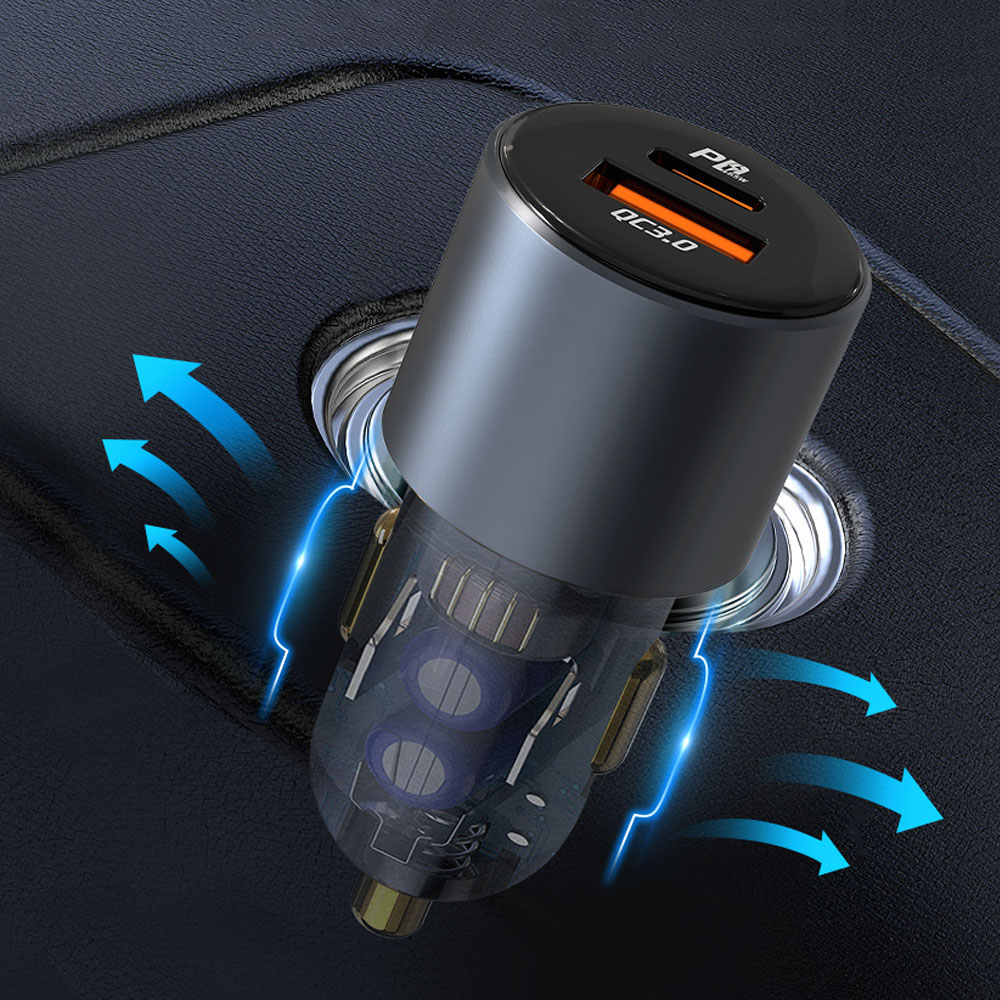 Zbliżenie ładowarki samochodowej z dwoma portami USB. Jest czarna i szara, włożona do gniazda zasilania samochodu. Niebieskie strzałki.