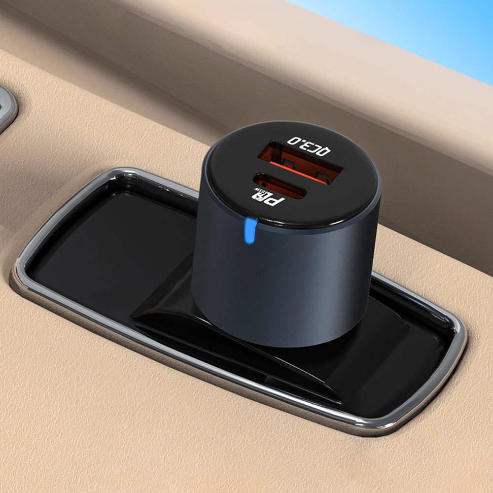Czarna ładowarka samochodowa USB z dwoma portami leży w czarnej tacy. Ładowarka wyświetla 'QC 3.0'. Tło jest beżowe.