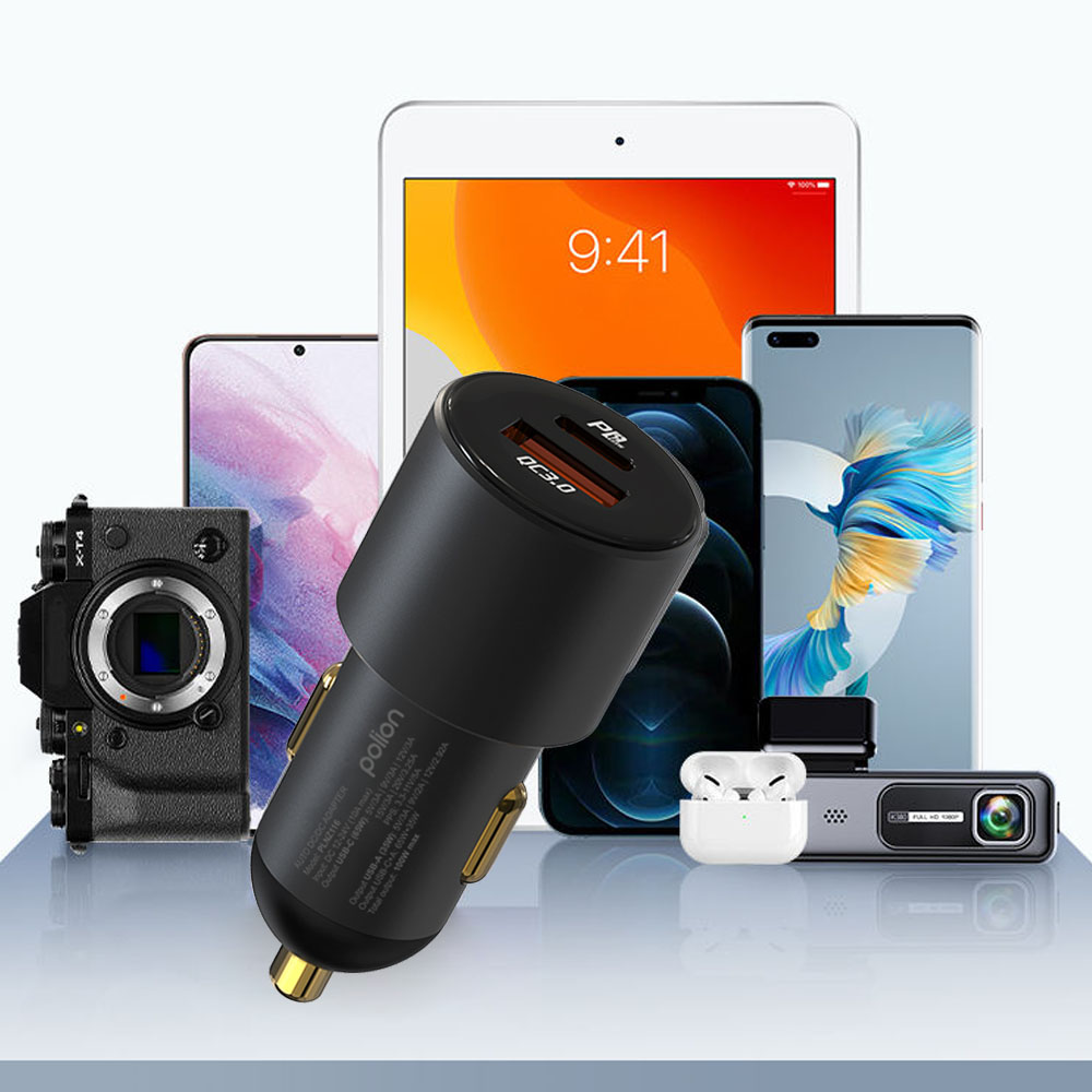 Ładowarka samochodowa z dwoma portami USB na pierwszym planie. Za nią widoczny jest tablet, telefony, aparat, słuchawki i kamera samochodowa.