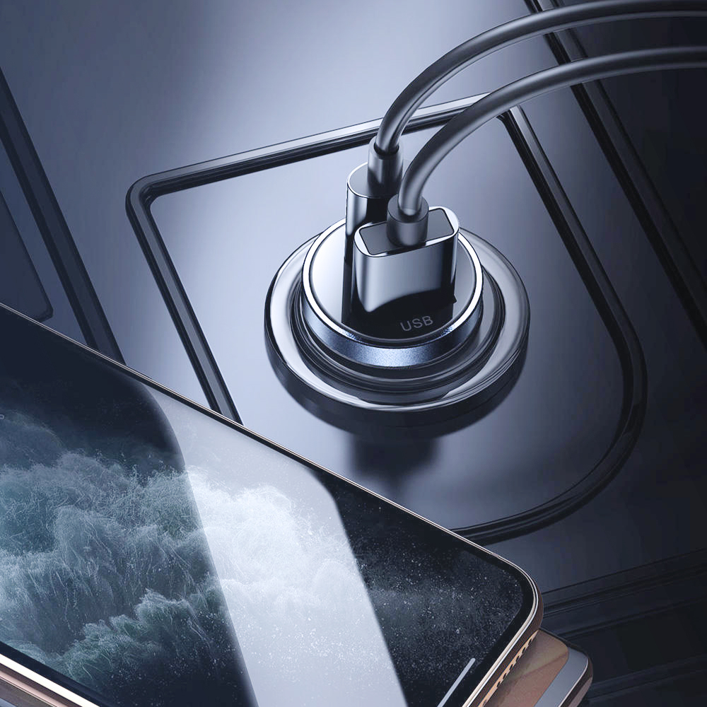 Telefon ładuje się kablem USB-C podłączonym do ładowarki samochodowej. Ładowarka jest srebrna, a telefon czarny.