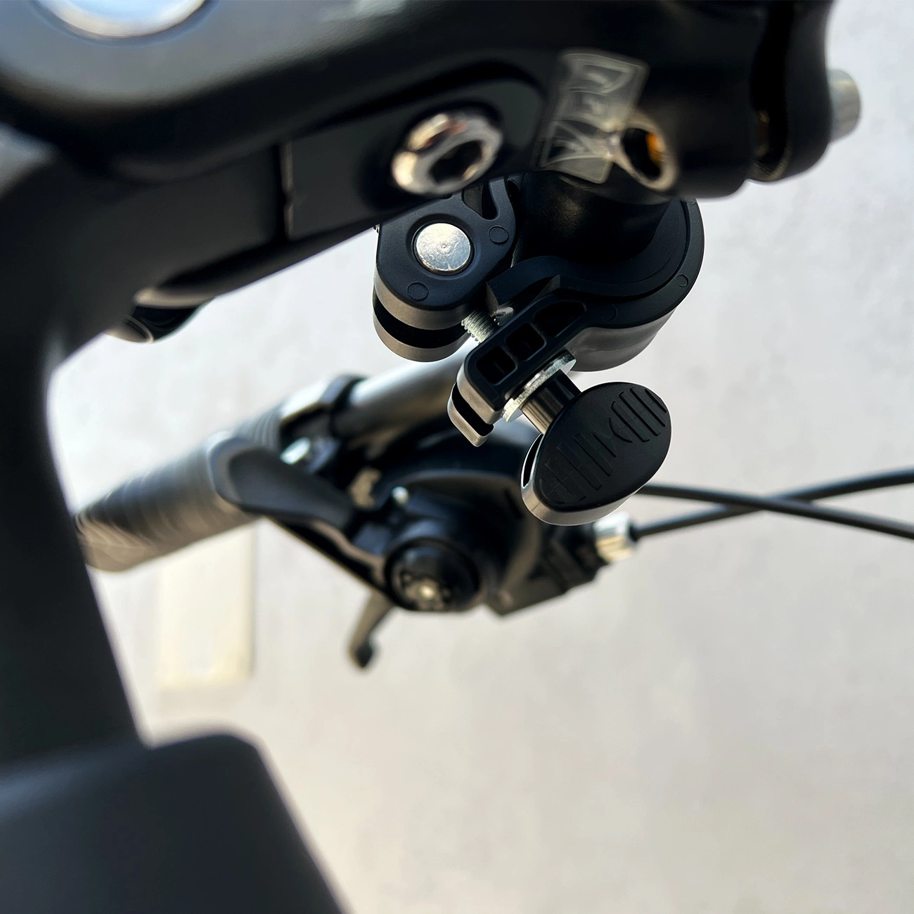 Nahaufnahme eines Fahrradlenkers mit schwarzen Griffen, Bedienelementen und einer schwarzen Zubehörhalterung. Der Hintergrund ist eine verschwommene Wand.