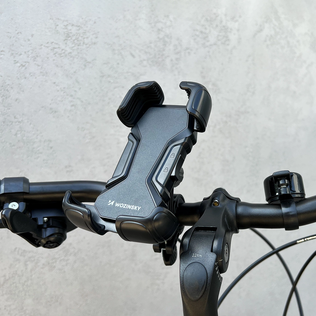 Ein schwarzer Telefonhalter ist an einem Fahrradlenker befestigt. Der Halter hat das Logo "Wozinsky". Eine Klingel und andere Fahrradteile sind sichtbar.