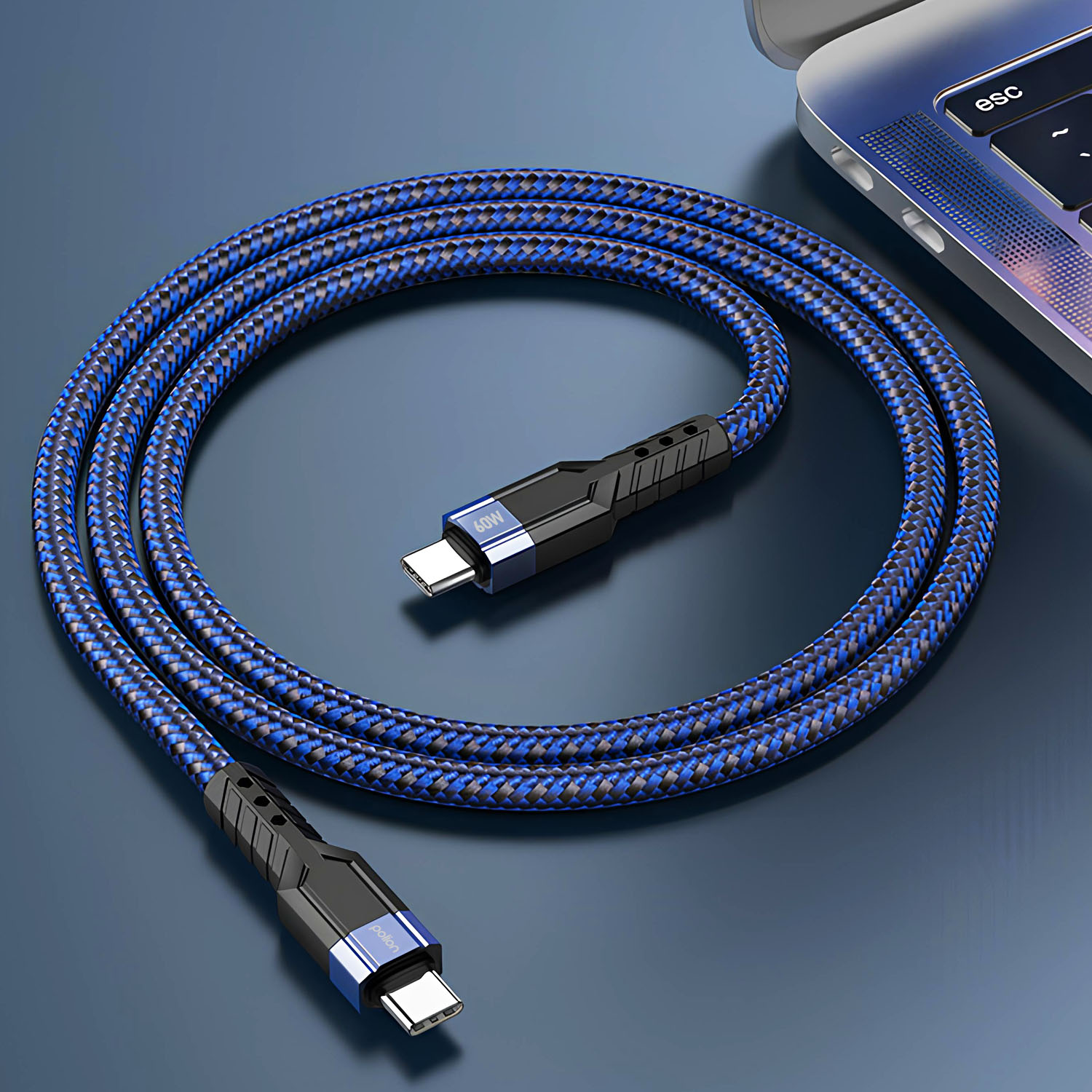 Niebiesko-czarny pleciony kabel USB-C, obok laptopa. Kabel jest zwinięty na niebieskiej powierzchni.