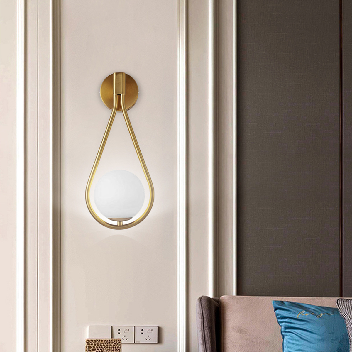 Eine goldene Wandleuchte mit Glaskugel hängt an einer cremefarbenen Wand. Rechts ist eine braune Wand. Darunter Steckdosen.