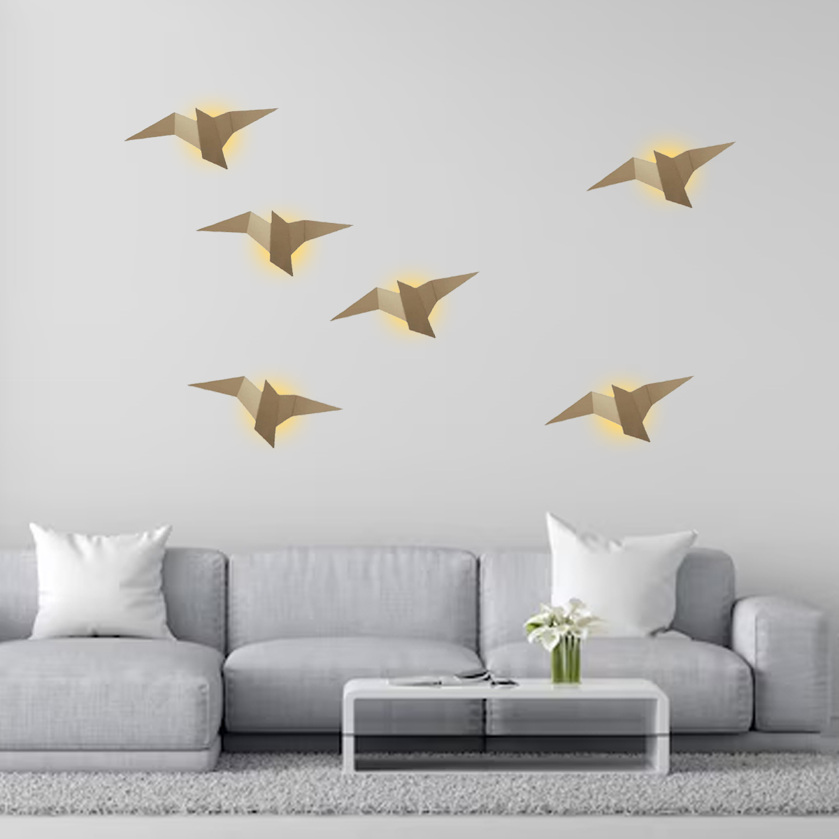 Origami-Vogellampen über einem grauen Sofa mit weißen Kissen. Davor steht ein weißer Tisch mit Blumen.