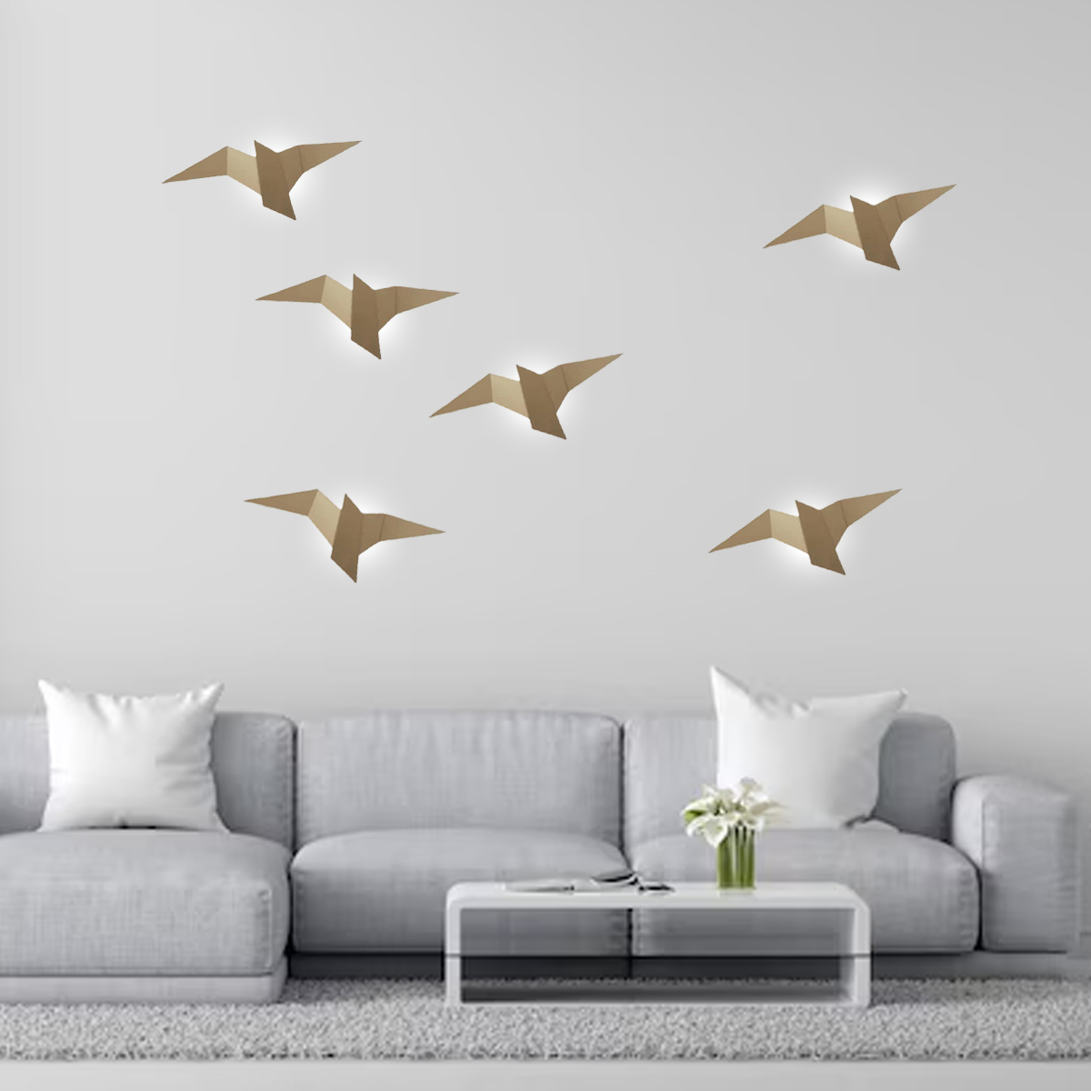 Wohnzimmer mit Papier-Vogellichtern an der Wand. Ein graues Sofa, weiße Kissen, ein weißer Tisch und Blumen sind im Raum.