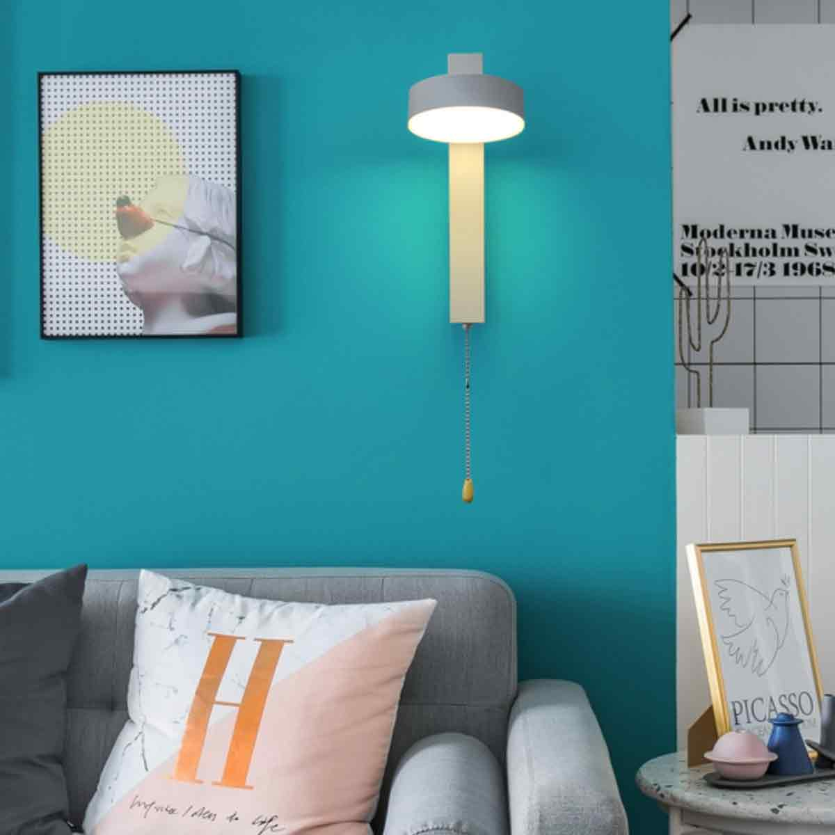 Eine türkisfarbene Wand mit Lampe und Kunst. Im Vordergrund befindet sich ein Sofa mit Kissen. Ein weiterer Bilderrahmen steht auf einem Tisch.
