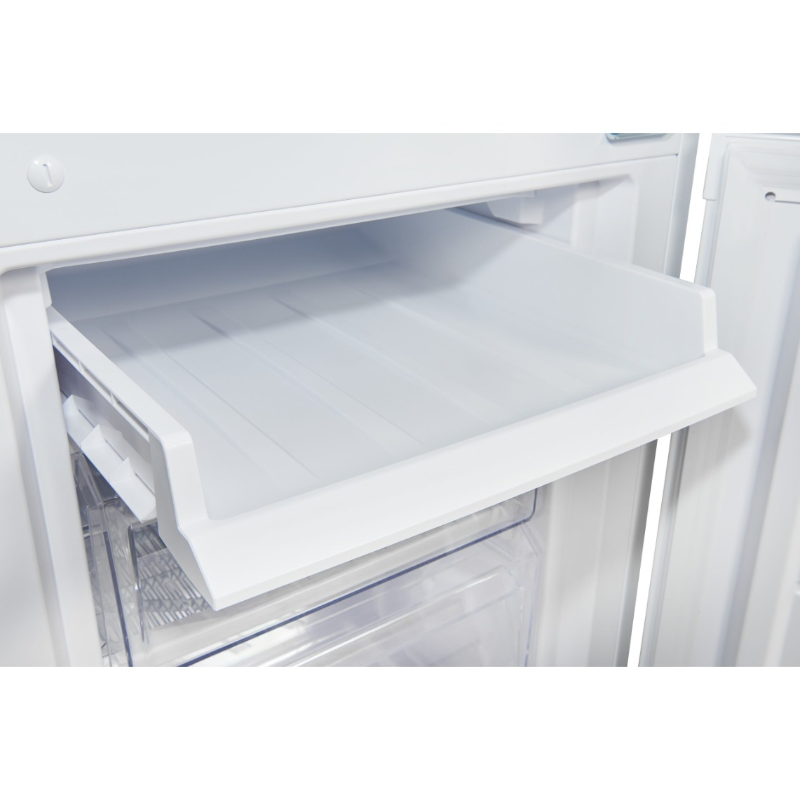 Primer plano de un refrigerador blanco abierto. El cajón superior está abierto, revelando una bandeja de plástico blanco vacía. Plástico transparente debajo.