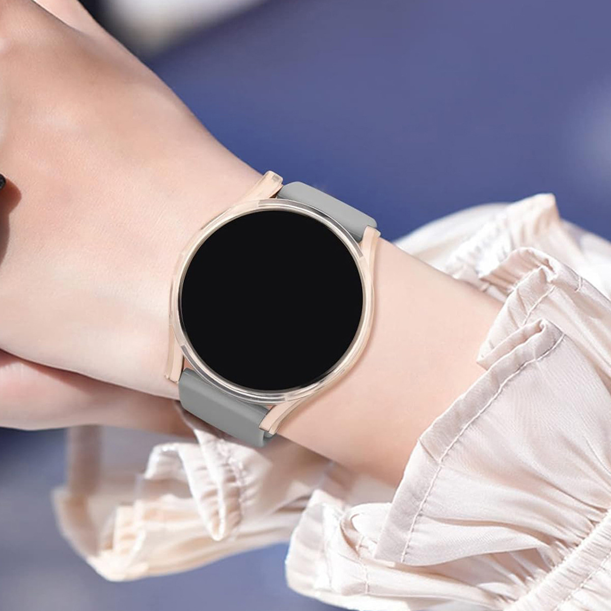Handgelenk mit Smartwatch. Die Uhr ist rund, goldfarben, mit grauem Band und schwarzem Bildschirm. Person trägt weißes Hemd.