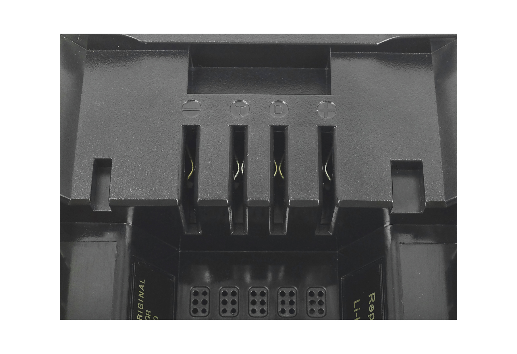 Nahaufnahme eines schwarzen Batterieanschlusses mit Symbolen und Anschlüssen. Gelbe Drähte sind in den Schlitzen sichtbar.