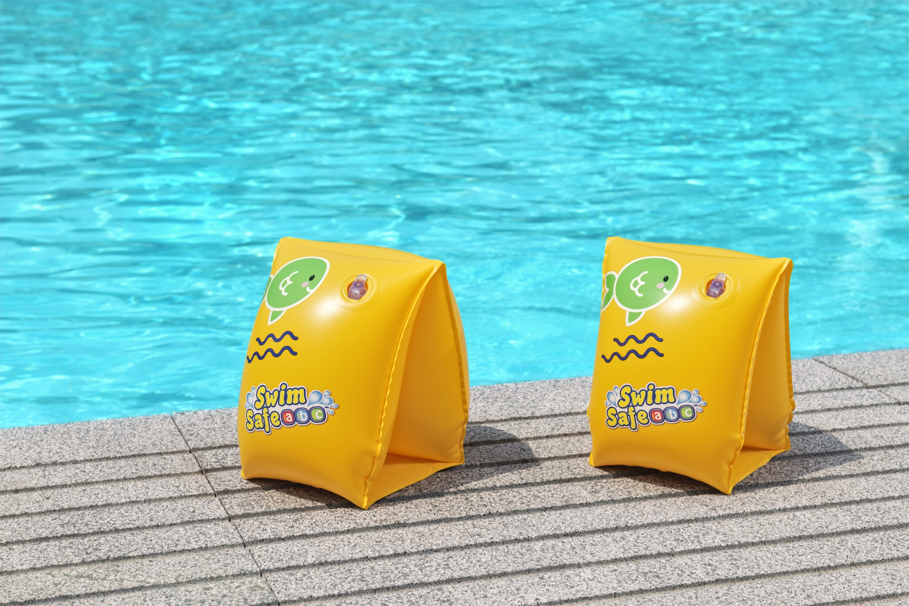 Zwei gelbe Schwimmflügel mit Fischdesign am Beckenrand. Poolwasser ist blau.