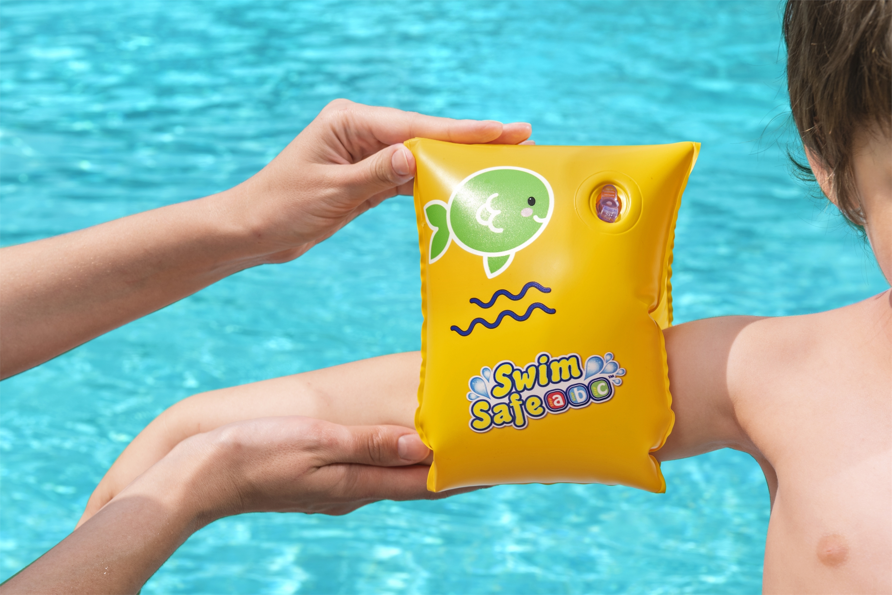 Ein gelber Schwimmflügel wird einem Kind von einem Erwachsenen angezogen. Im Hintergrund ist Poolwasser.