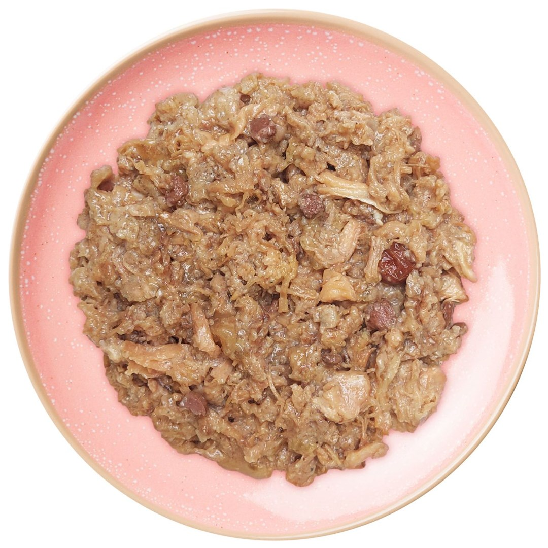 Różowy talerz z porcją mokrej karmy dla zwierząt. To mieszanka brązowych i beżowych składników, prawdopodobnie mięsa i warzyw.