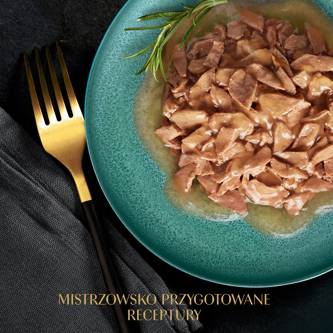 Na turkusowym talerzu gotowane mięso w sosie, udekorowane rozmarynem. W pobliżu złoty widelec i ciemna tkanina.