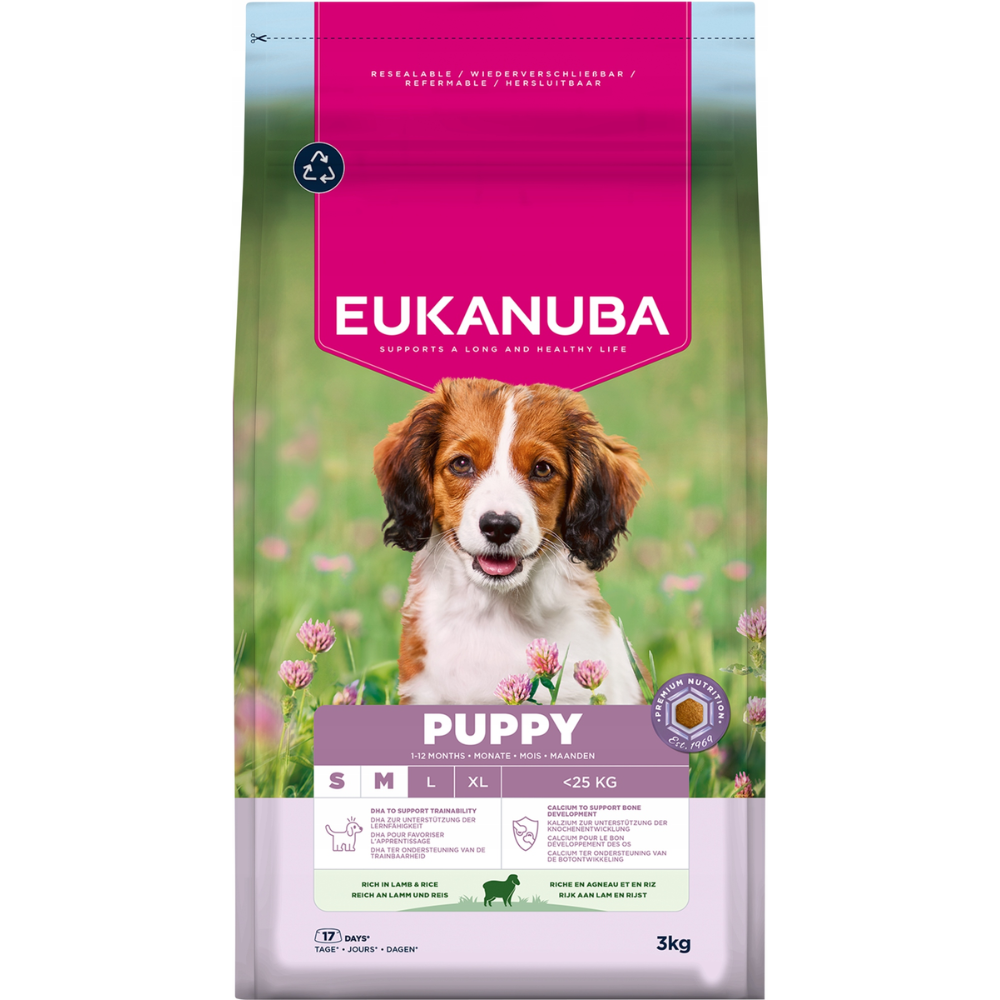 Torba z karmą dla psów z szczeniakiem, tekst 'Eukanuba', 'Puppy' i inne szczegóły. Tło z zielonej trawy i kwiatów.