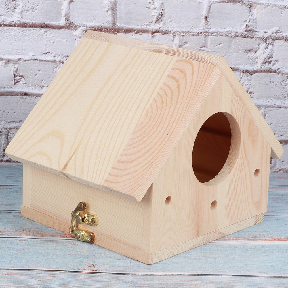 Ein hölzernes Vogelhaus mit rundem Eingangsloch und goldenem Verschluss. Es steht auf einer blau-weißen Oberfläche, eine Ziegelmauer im Hintergrund.