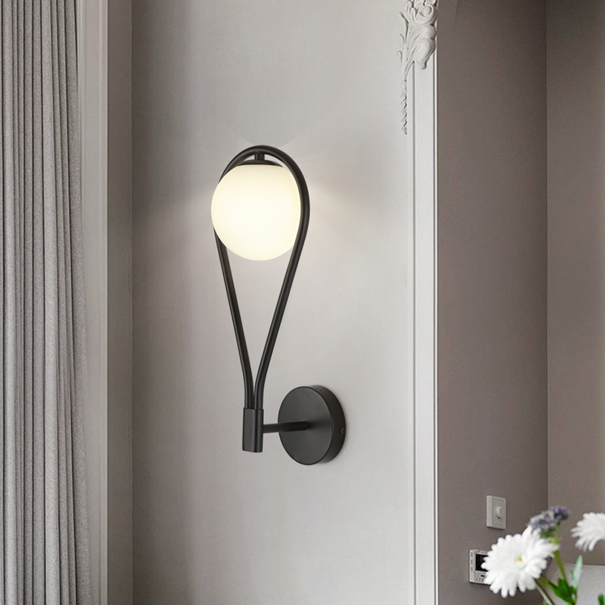 Eine moderne schwarze Wandleuchte mit kugelförmigem Licht, an einer grauen Wand montiert. Dekorative Details und Vorhänge sind im Hintergrund zu sehen.