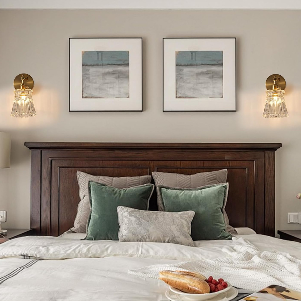 Schlafzimmer mit Bett, Kissen, Kunst und Wandleuchten. Ein Teller mit Essen liegt auf dem Bett. Dunkles Holz-Kopfteil und Akzente.